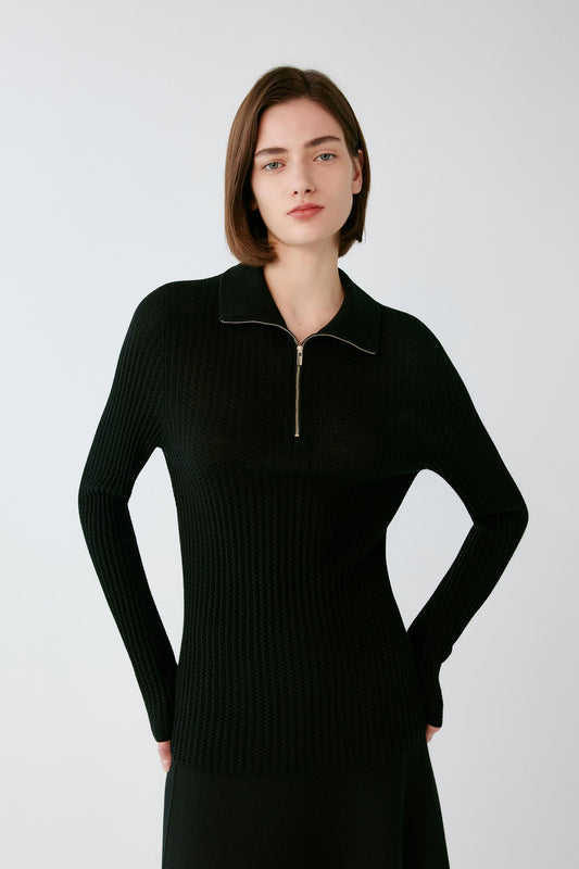 Front view of a woman wearing a deep black worsted wool pullover, showing the zip neckline, pointed collar and fitted silhouette.