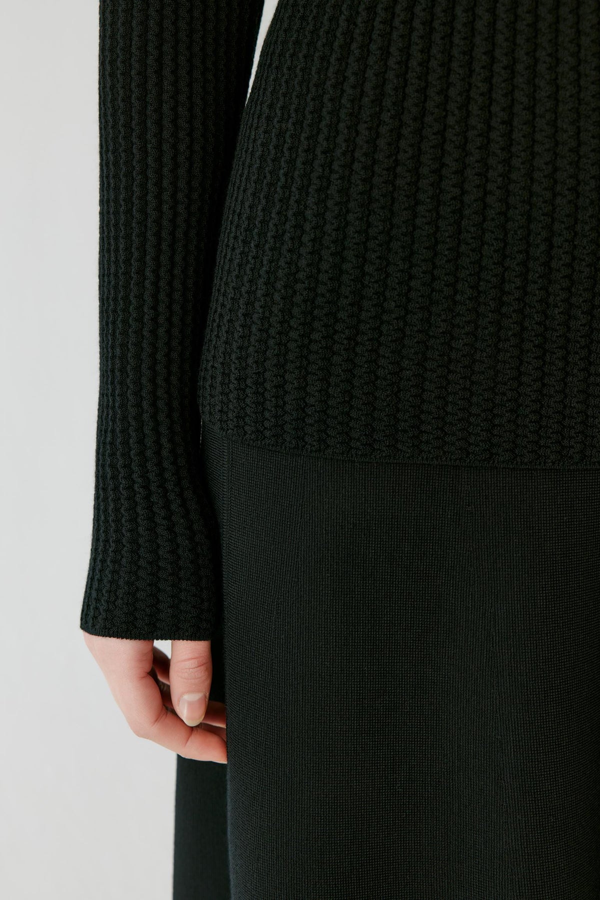 Close-up highlighting the long sleeve and ribbed knit texture of the deep black worsted wool pullover.