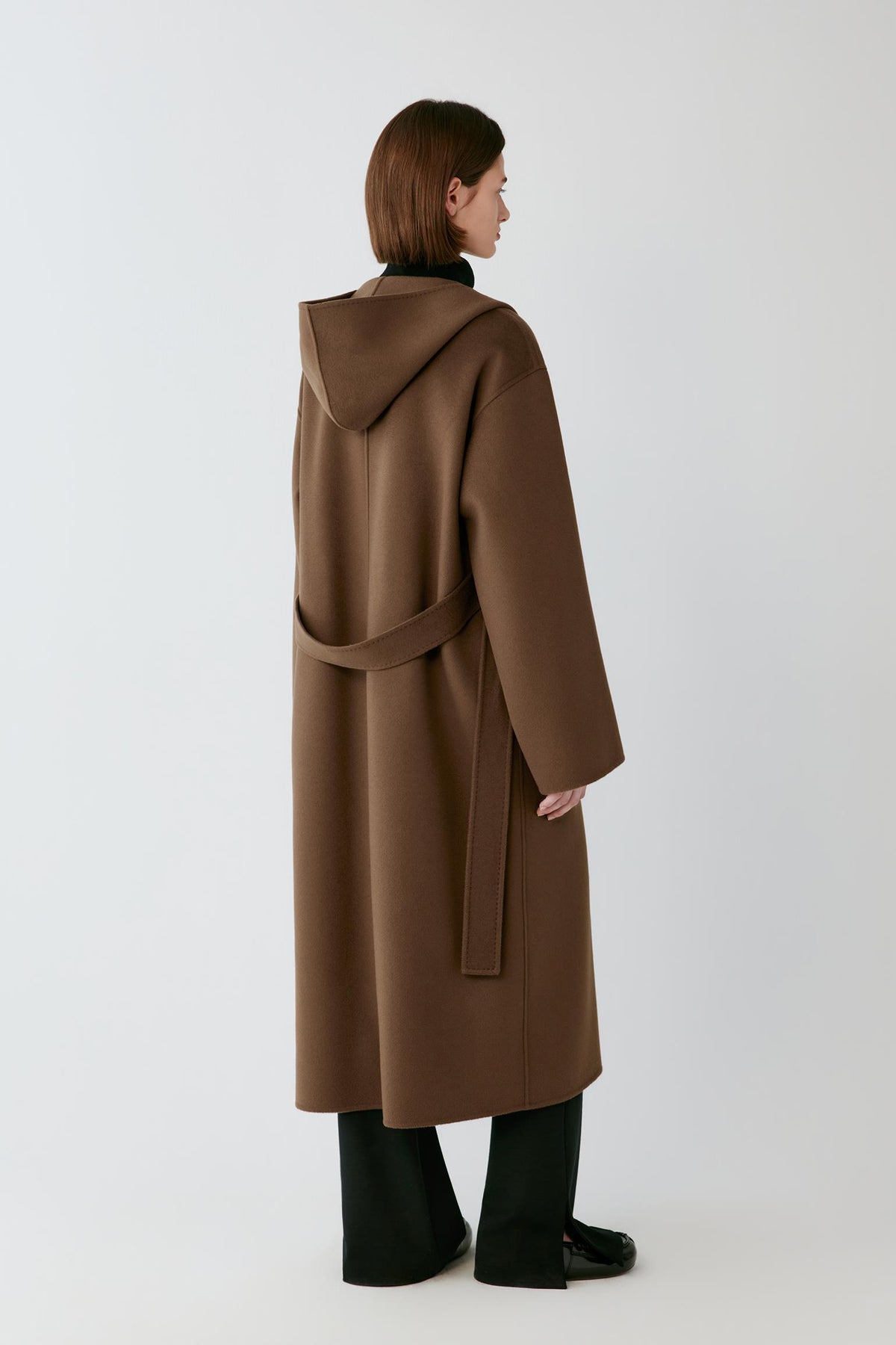 Back view of a woman wearing the rich brown double-face wool and cashmere coat, showing the hood and long straight silhouette.