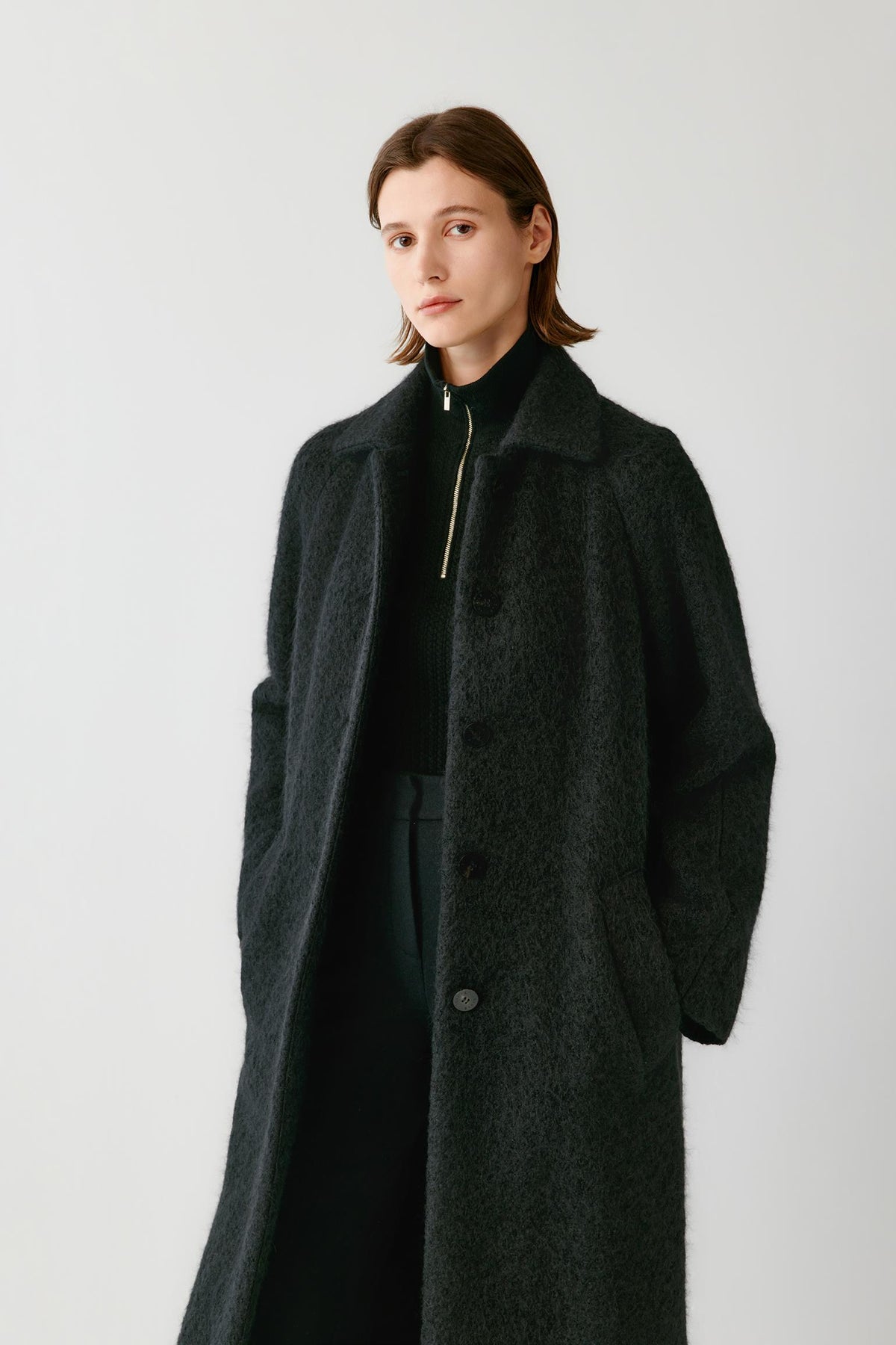 Front view highlighting the pointed collar, concealed front fastening and brushed tweed texture of the deep black coat.