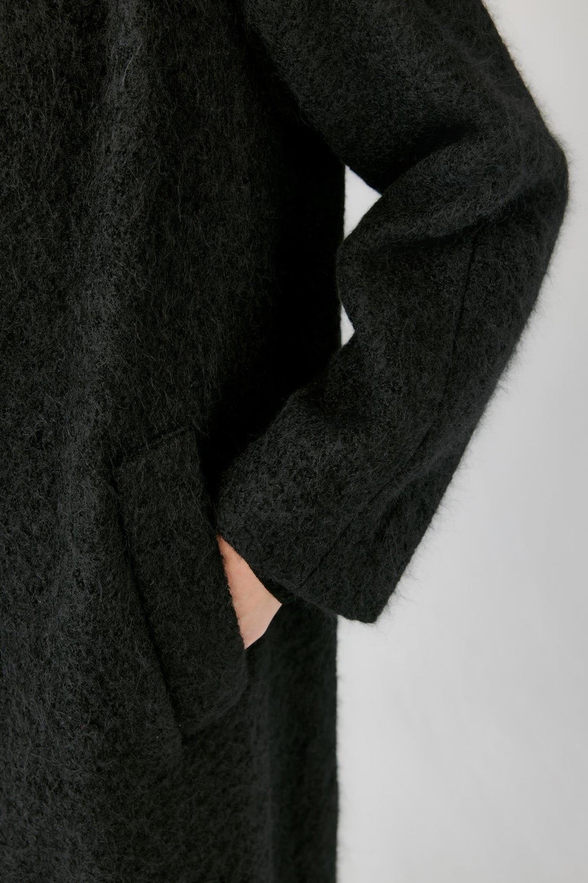 Close-up highlighting the side pocket, sleeve and brushed tweed texture of the deep black coat.