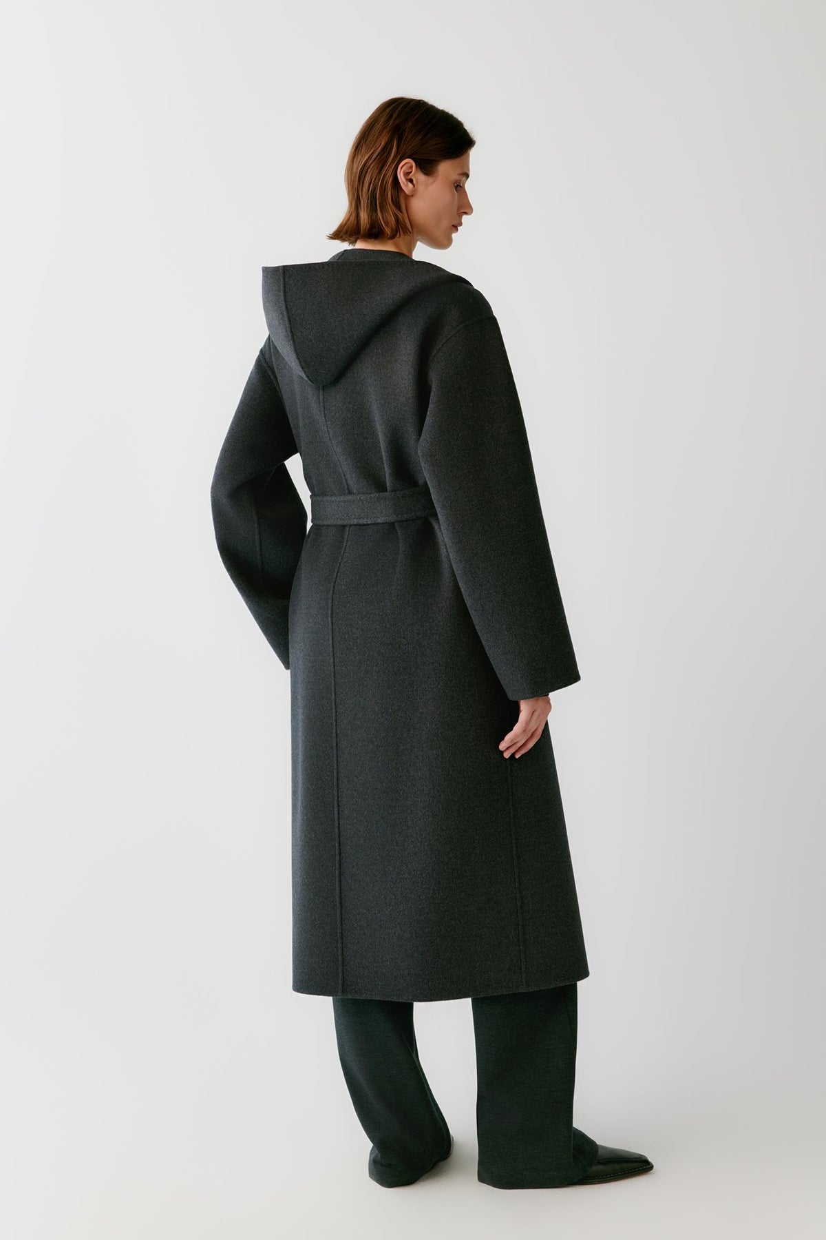 Back view of a woman wearing the dark grey melange double-face wool and cashmere coat, showing the long silhouette and clean construction.