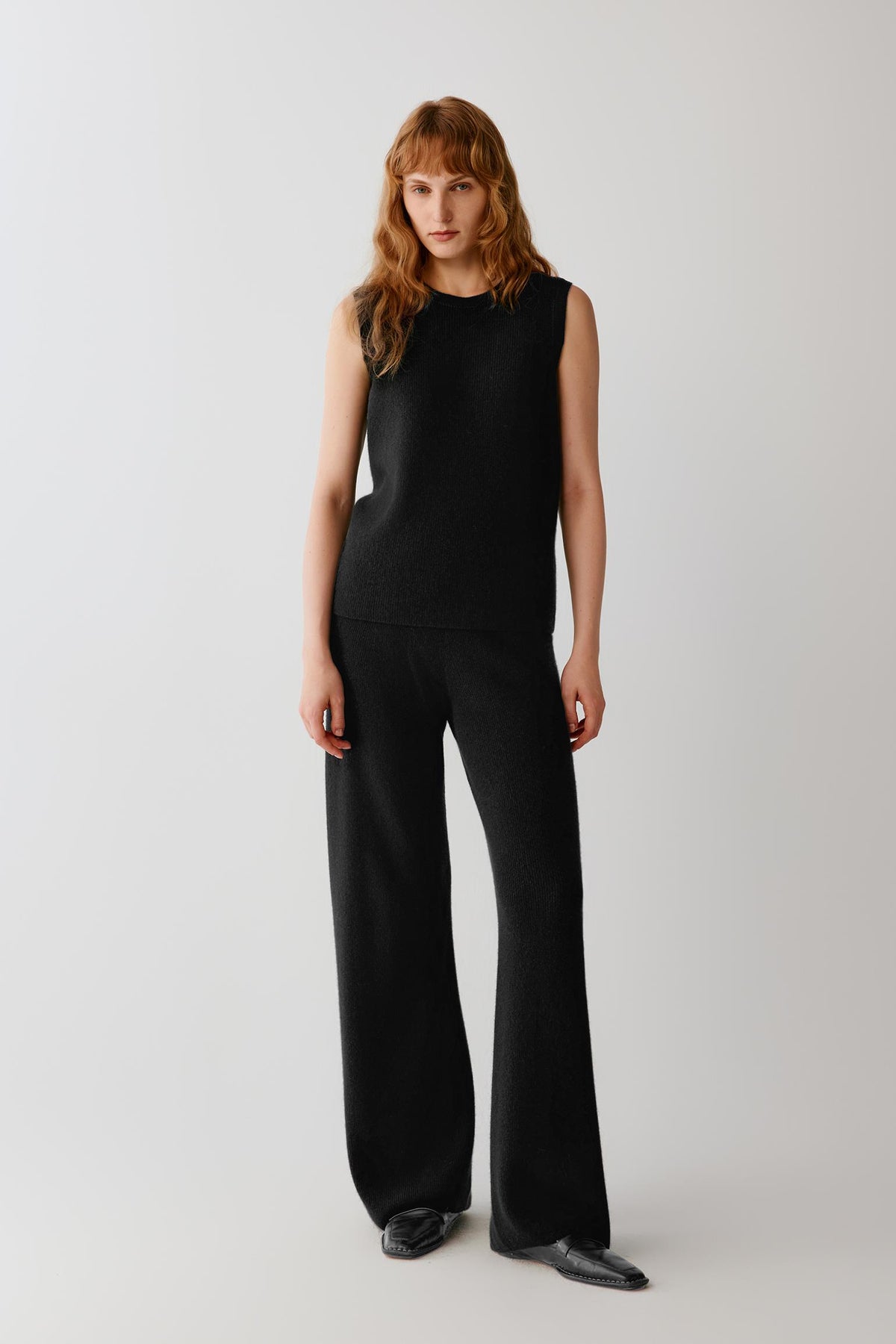 Front view of a woman wearing black cashmere trousers, showing the high-rise waist and straight-leg silhouette.