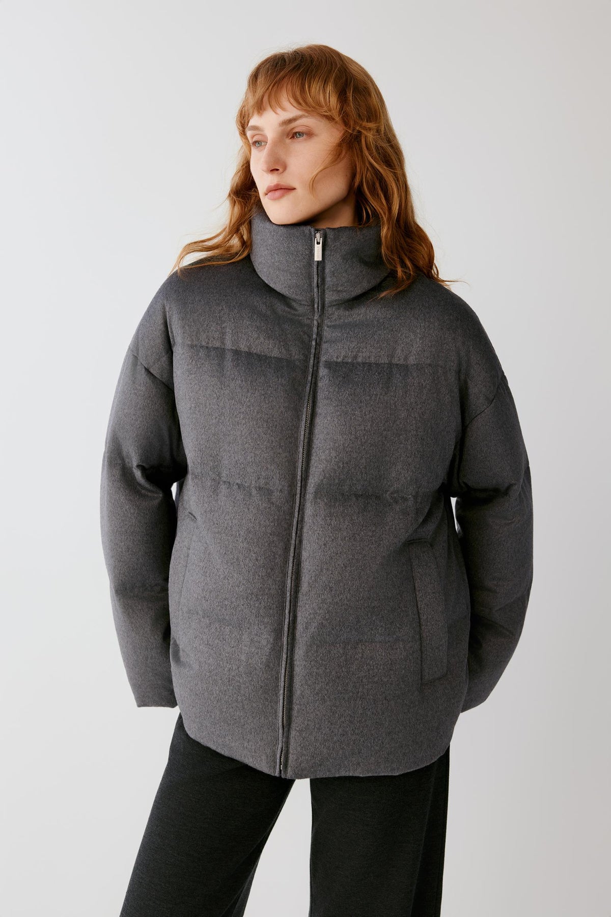 Front view of a woman wearing a dark grey melange silk tweed down coat, showing the high stand collar, quilted construction and relaxed silhouette.