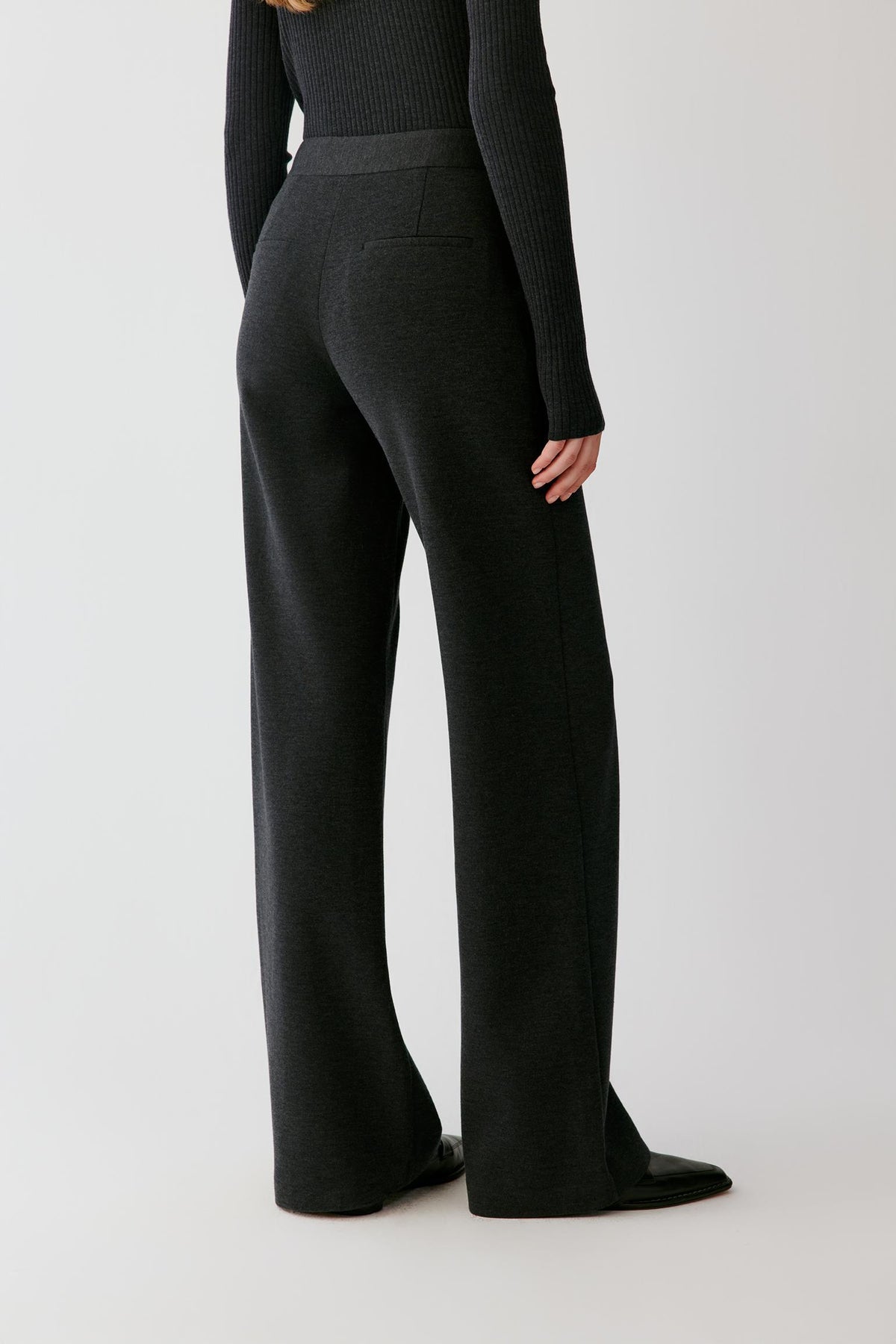 Three-quarter view showing the straight-leg silhouette and smooth jersey construction of the dark grey melange trousers.