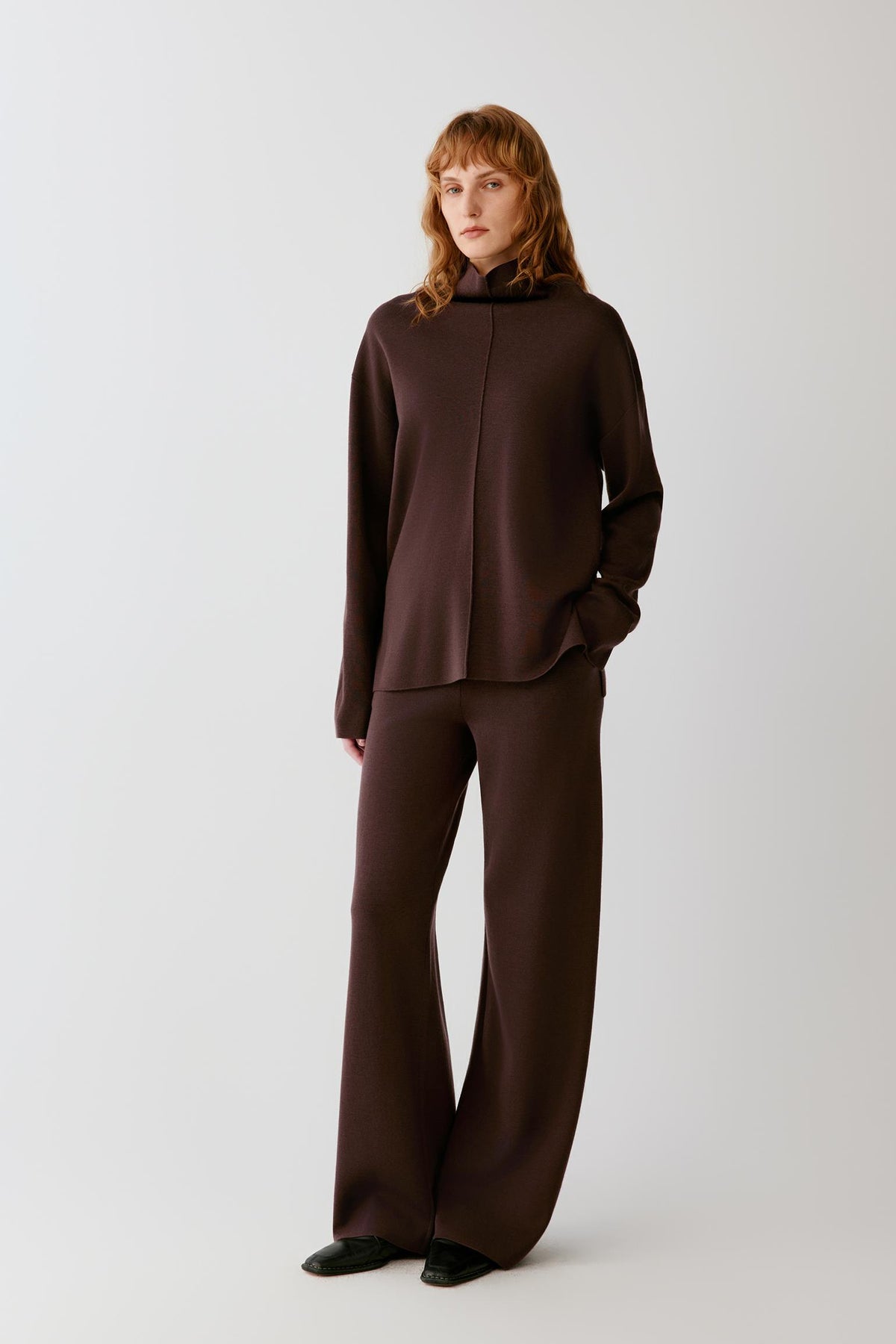 Full-length view of a woman wearing the dark brown merino wool pullover, highlighting the straight fit and long sleeves.