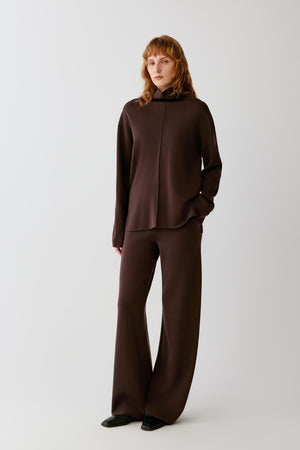 Full-length view of a woman wearing the dark brown merino wool pullover, highlighting the straight fit and long sleeves.
