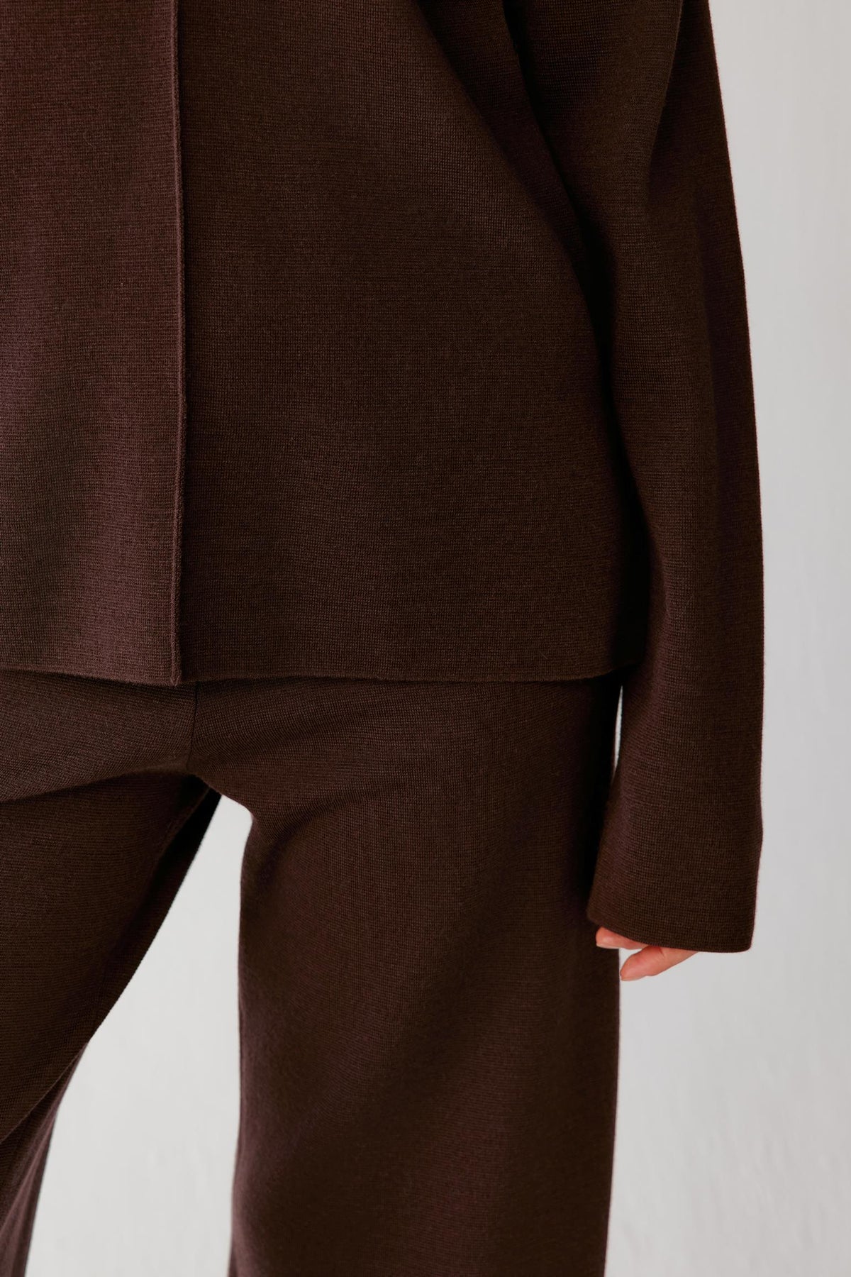 Close-up highlighting the straight hem, long sleeve and smooth dark brown merino wool knit.