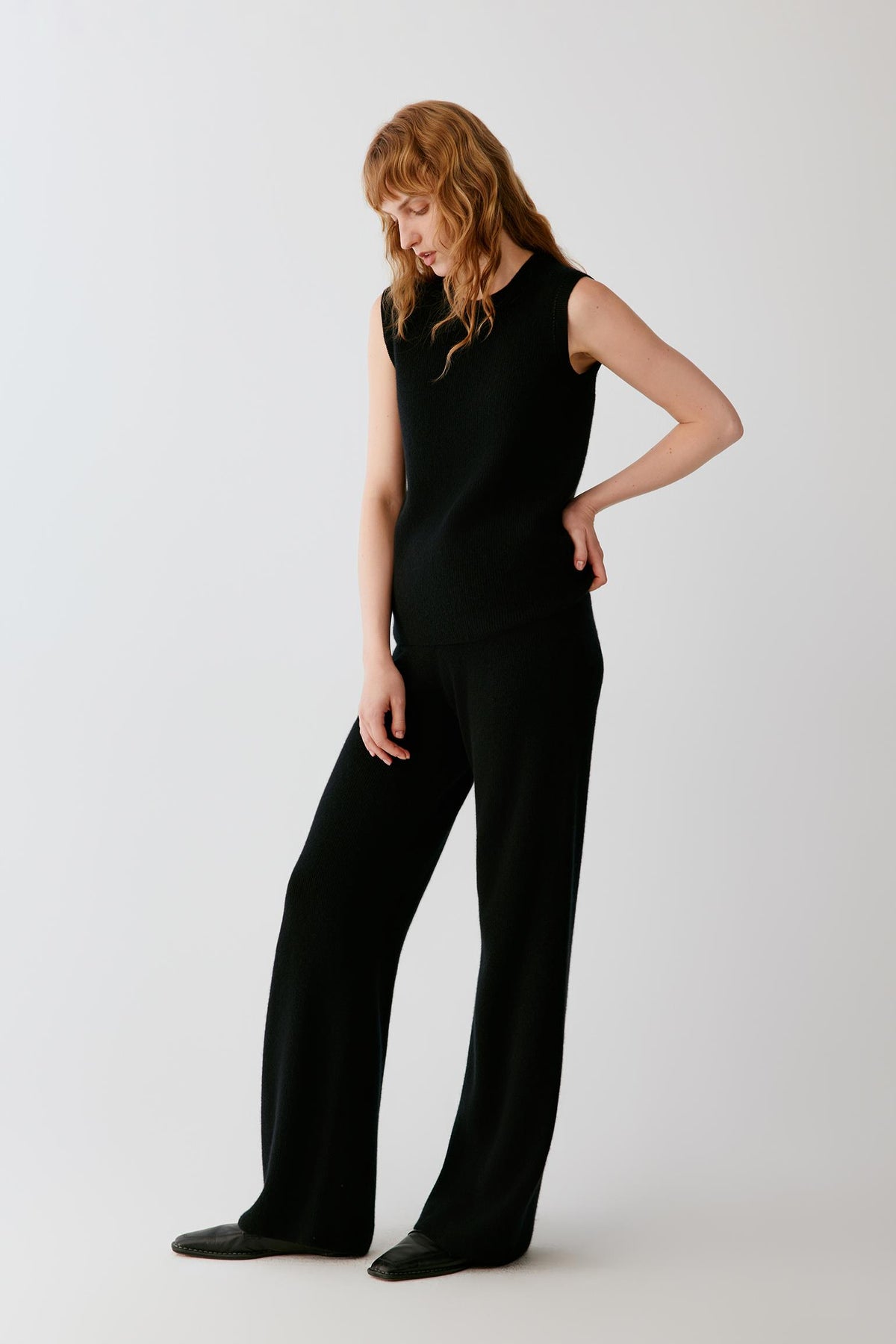 Three-quarter view of a woman wearing the black cashmere trousers, showing the straight-leg cut and fluid drape.