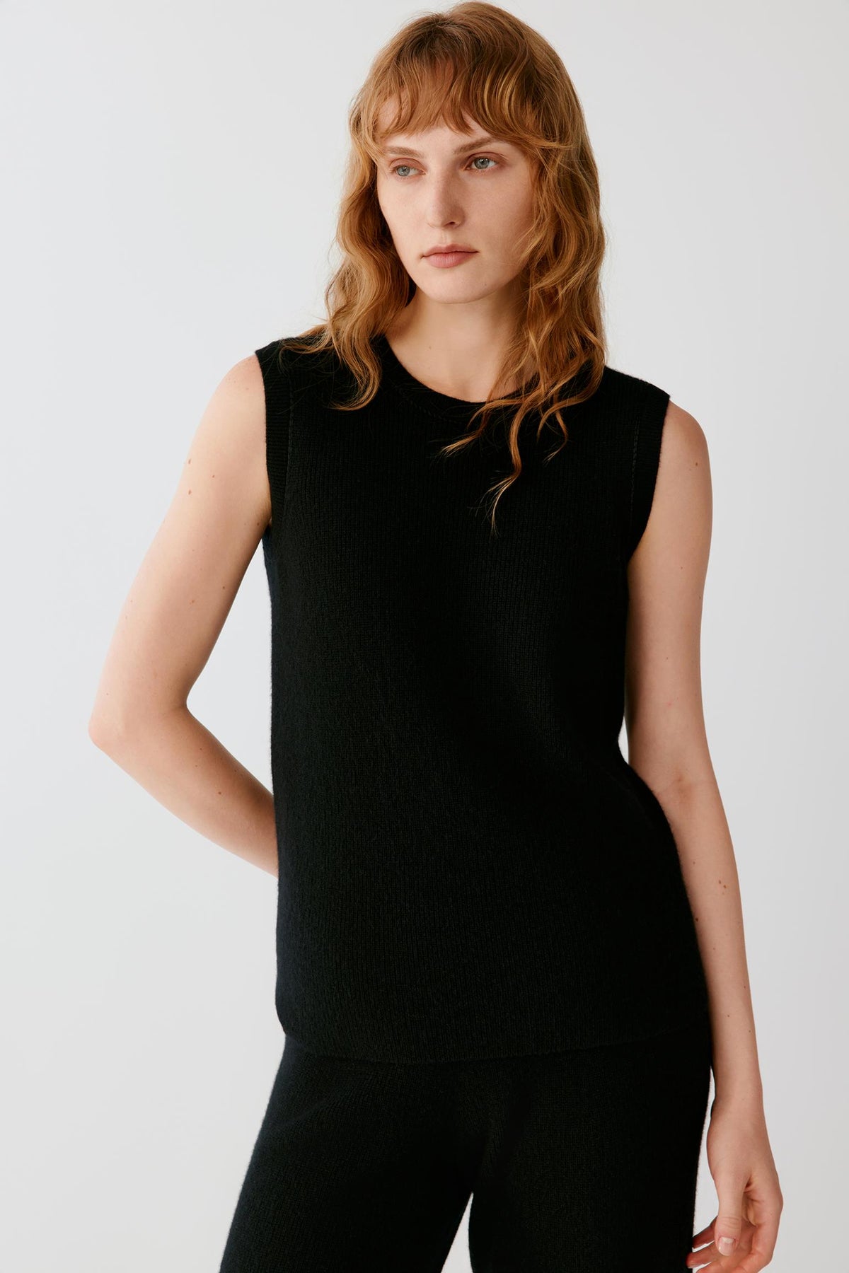 Front view of a woman wearing a black sleeveless cashmere pullover, showing the round neckline, wide armholes and straight silhouette.