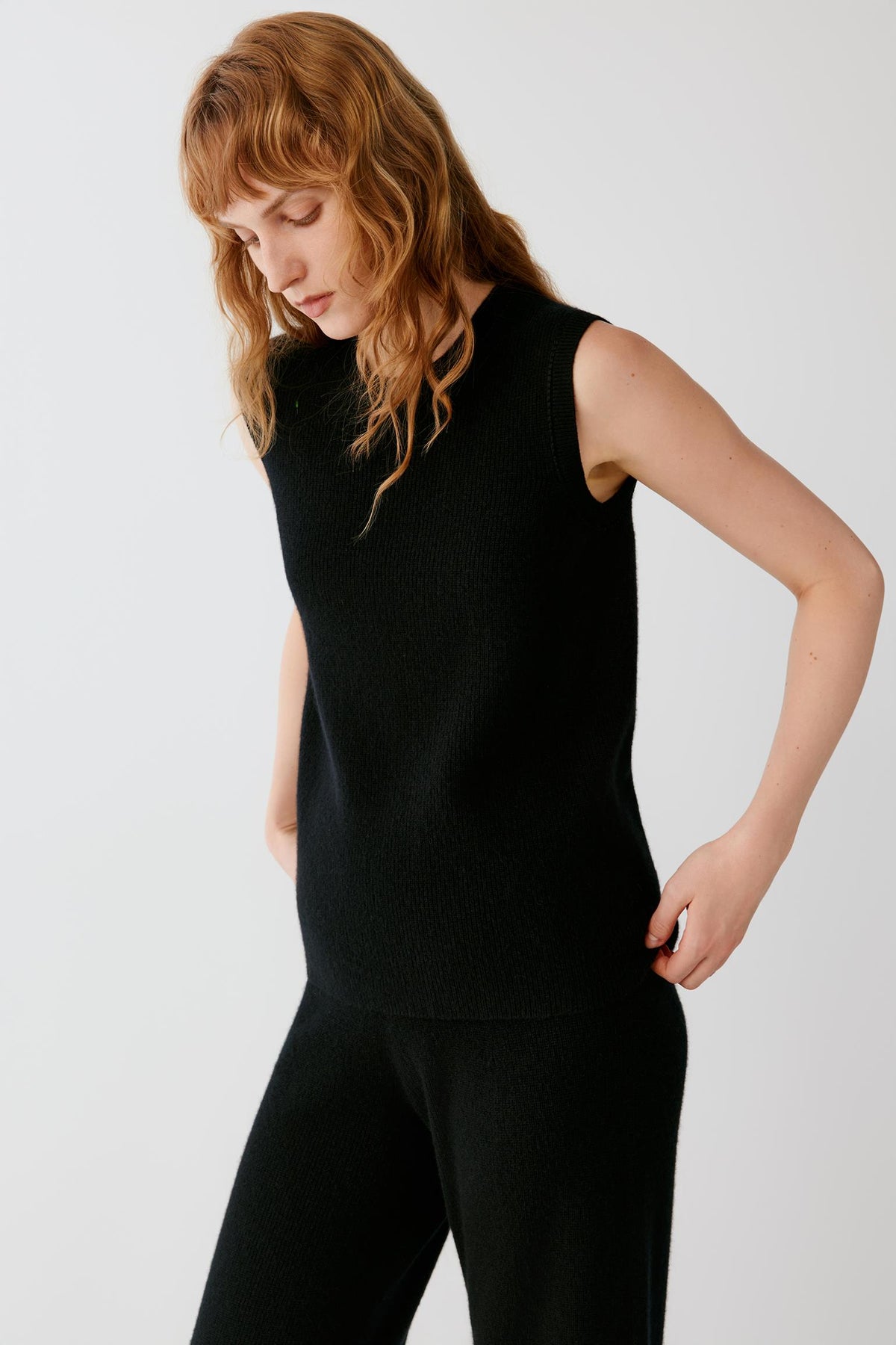 Three-quarter view of a woman wearing the black sleeveless cashmere pullover, highlighting the wide armholes and fitted shoulder line.