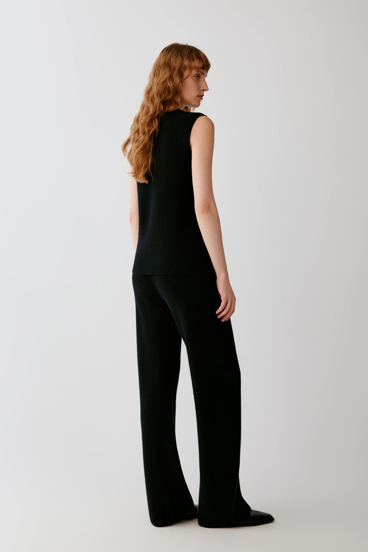Side view of a woman wearing the black sleeveless cashmere pullover, showing the sleeveless cut and straight silhouette.
