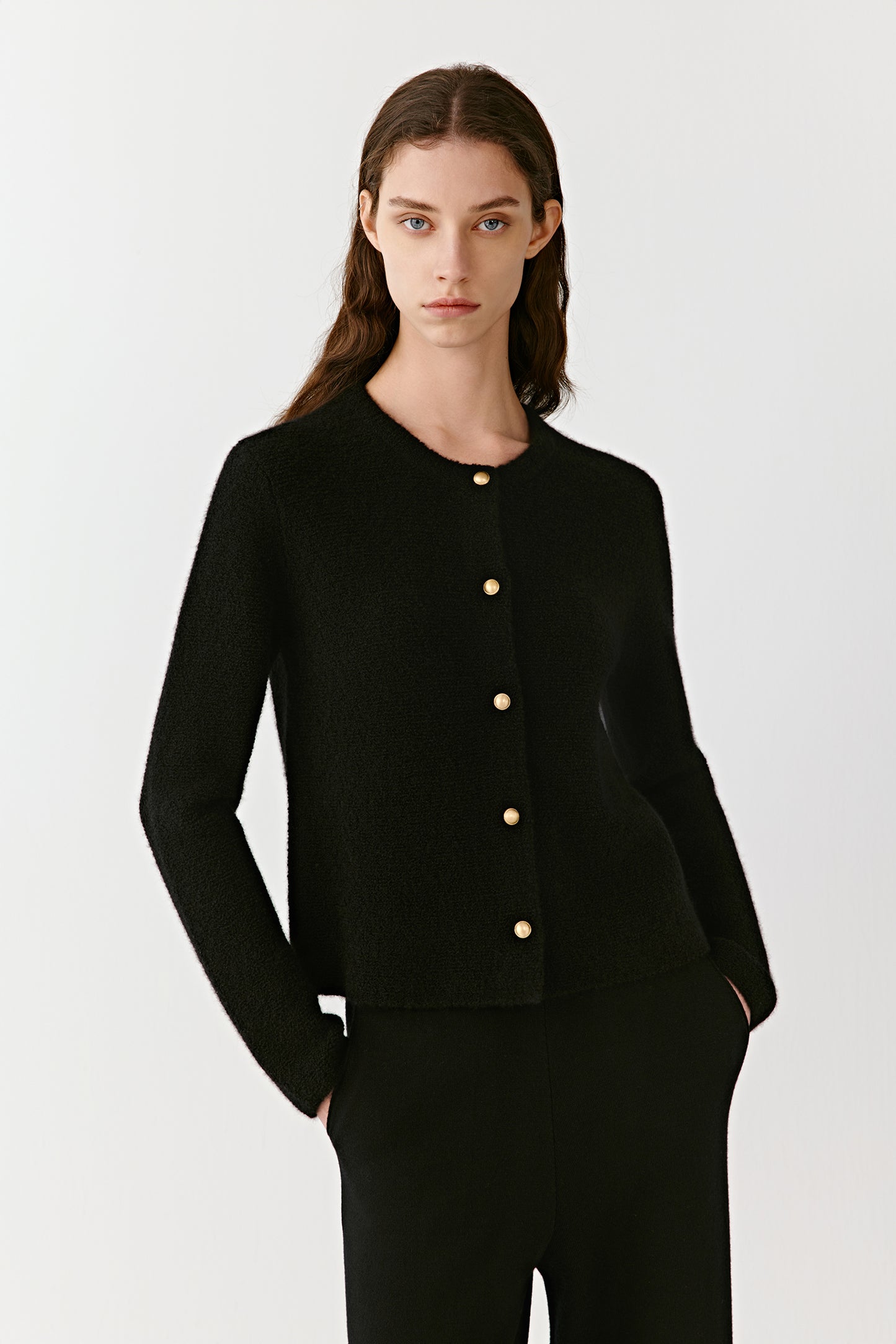 Three-quarter view of a person wearing a black cashmere cardigan with metal buttons, highlighting the slim fit and long sleeves. The model stands against a plain backdrop with relaxed posture