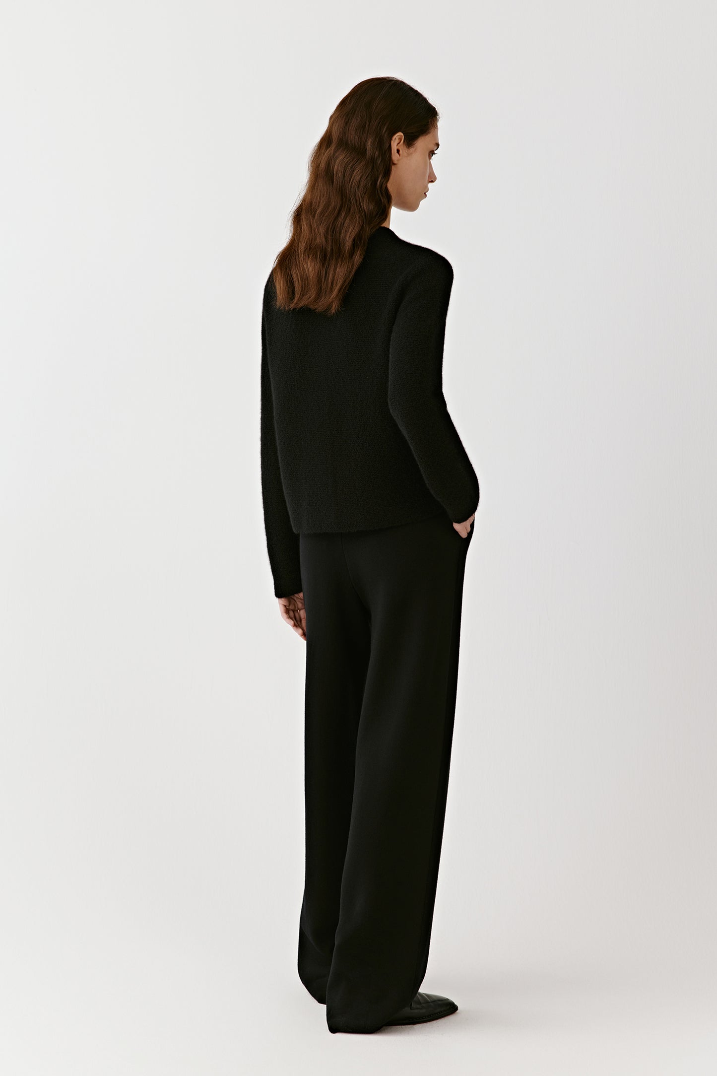 Side view of a person wearing black wide-leg merino wool trousers, highlighting the relaxed, flowing silhouette.
