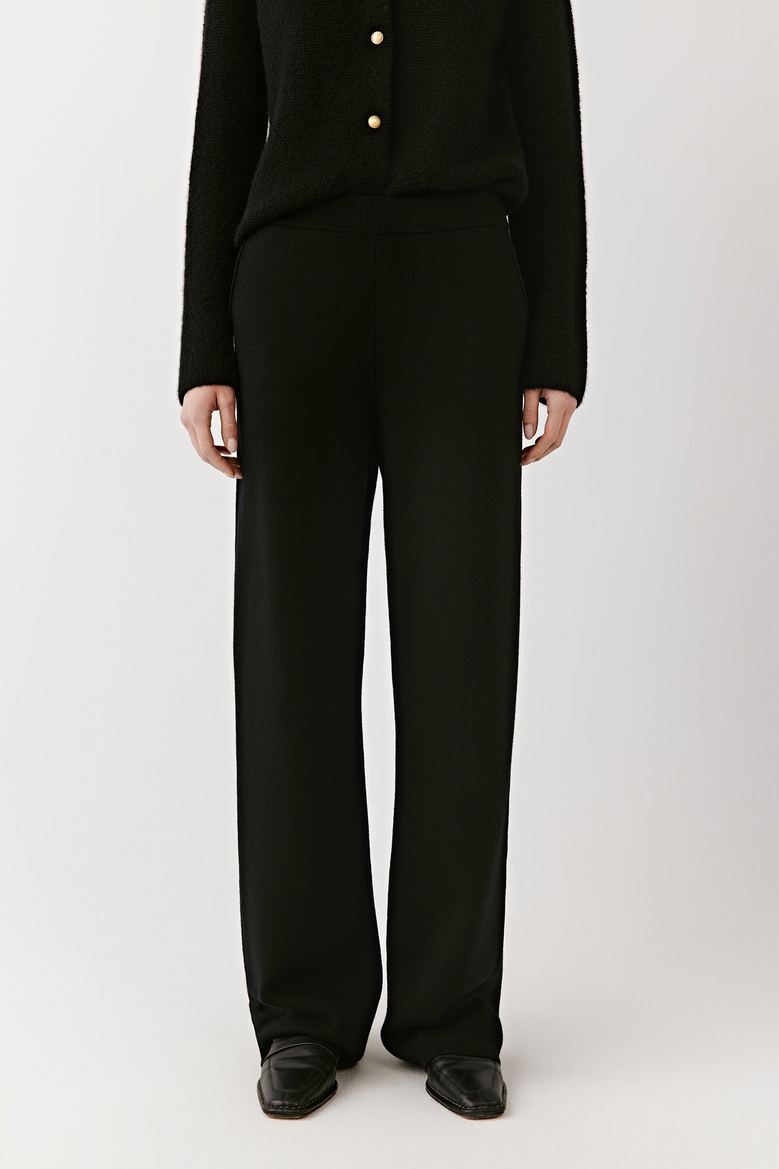 Front close-up from waist to ankle of black wide-leg merino wool trousers, showing the straight cut and dense weave.