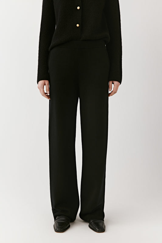Front close-up from waist to ankle of black wide-leg merino wool trousers, showing the straight cut and dense weave.