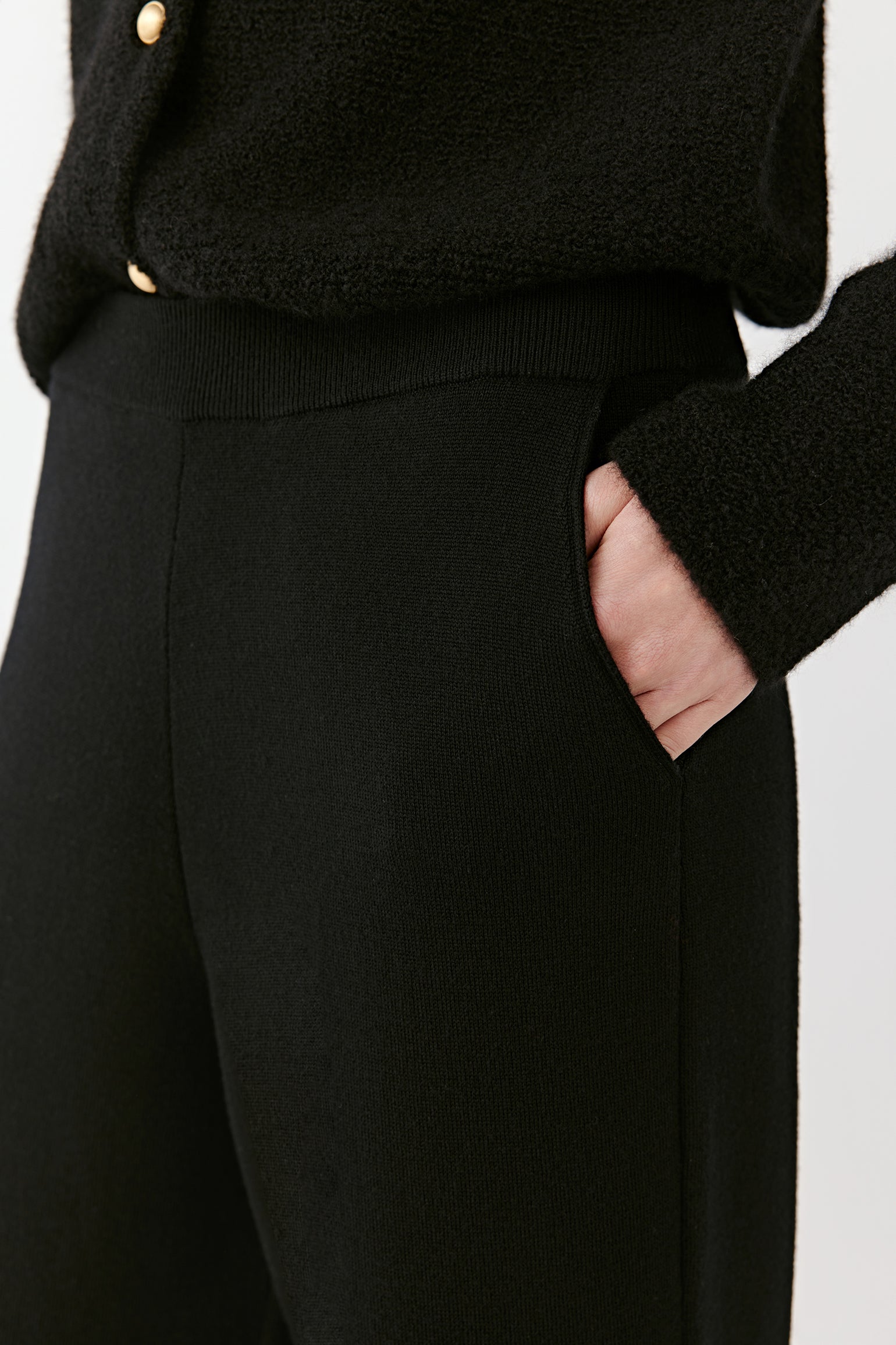 Close-up of the upper section of black wide-leg merino wool trousers, focusing on the waistband, pocket detail, and soft dense weave.