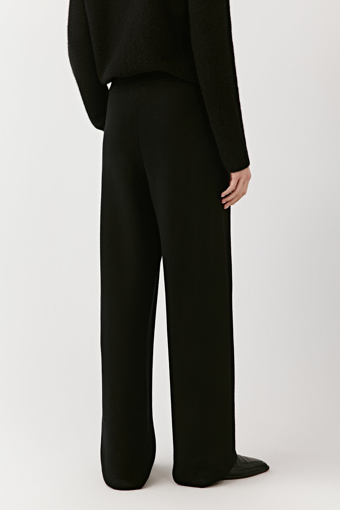 Full-length back view of black wide-leg merino wool trousers, showing the fit, drape, and elongated lines.