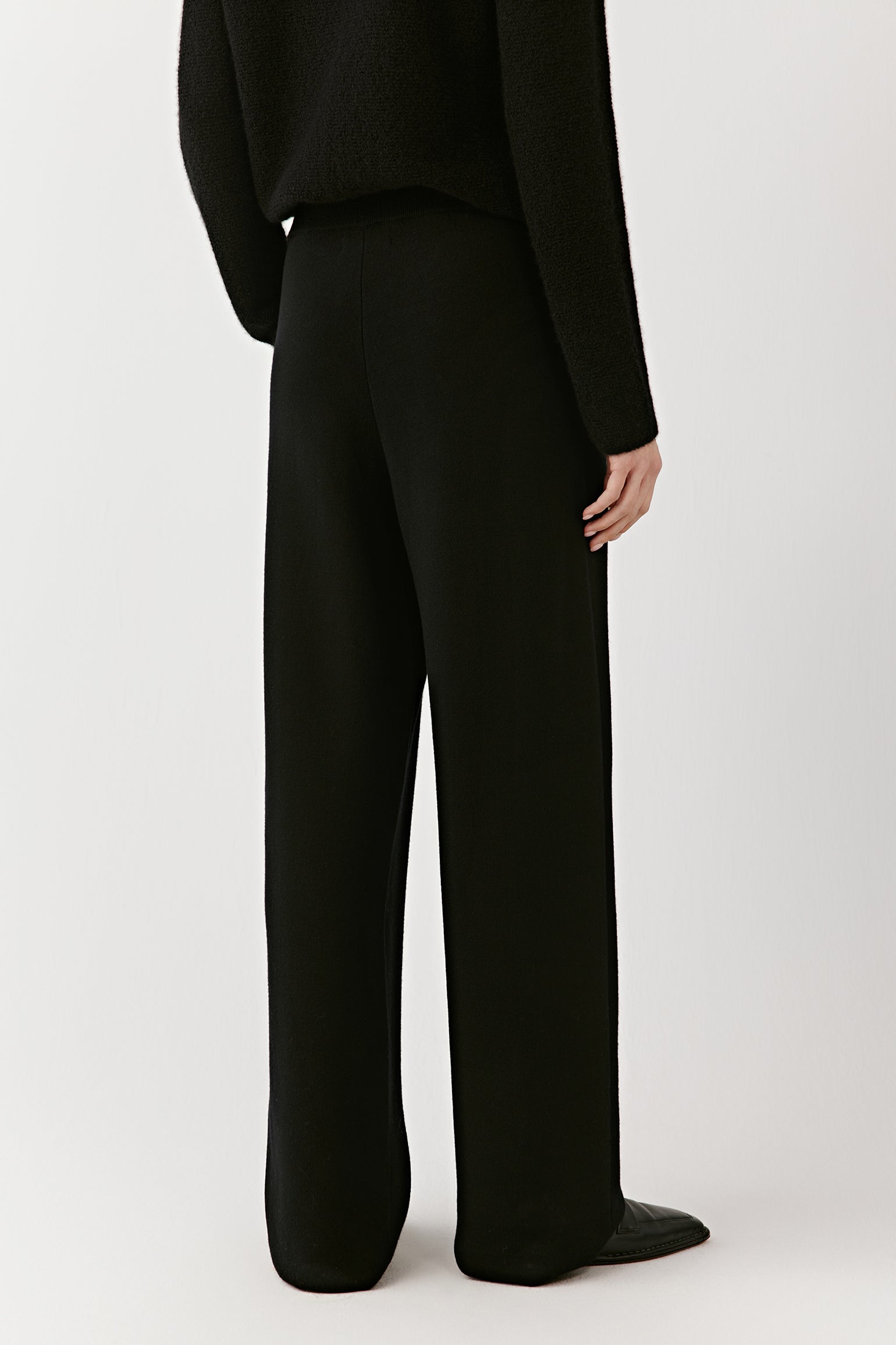 Full-length back view of black wide-leg merino wool trousers, showing the fit, drape, and elongated lines.