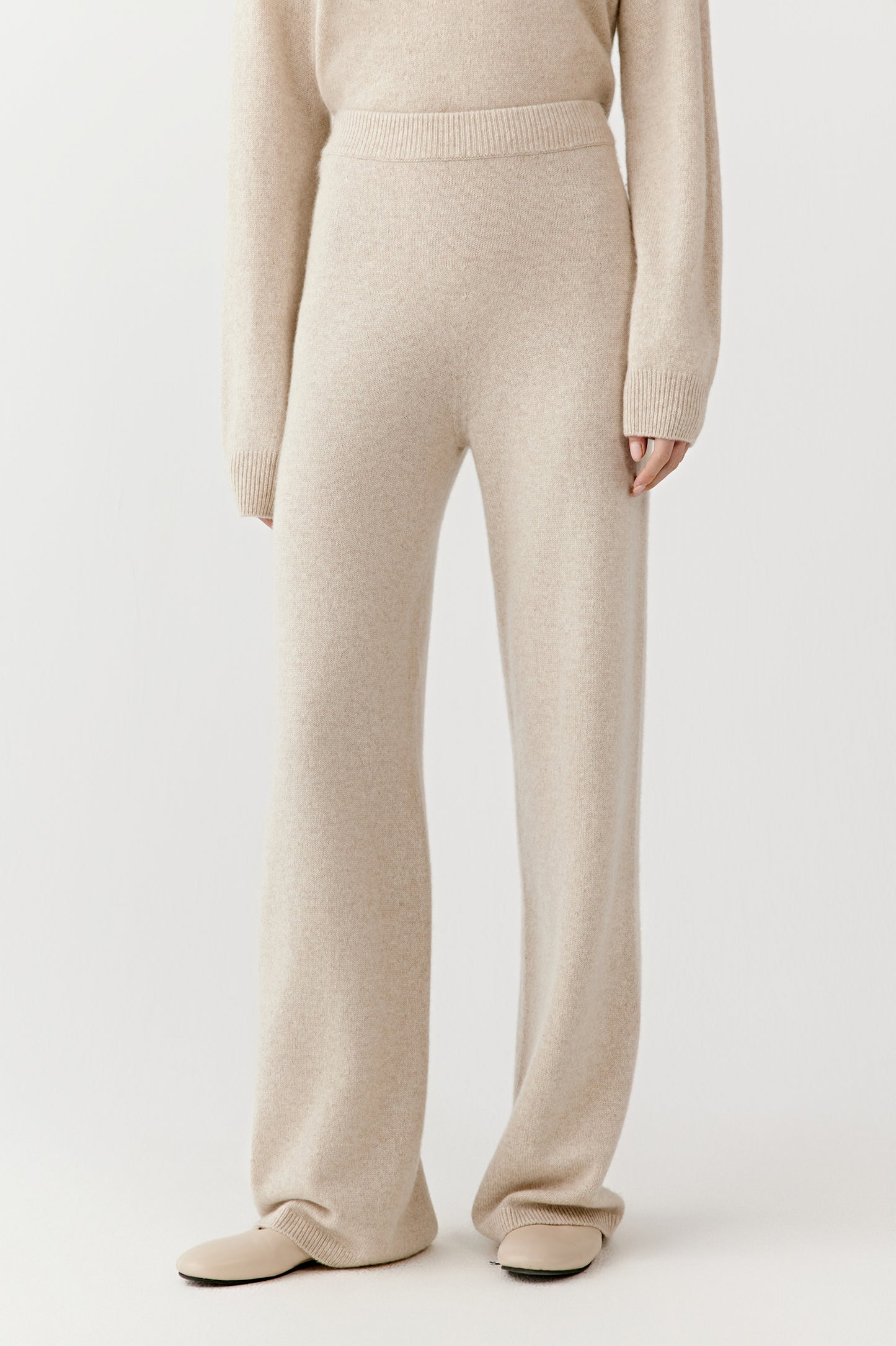 Close-up from waist to ankle showing the cream cashmere trousers’ straight-leg cut, soft texture, and clean lines.