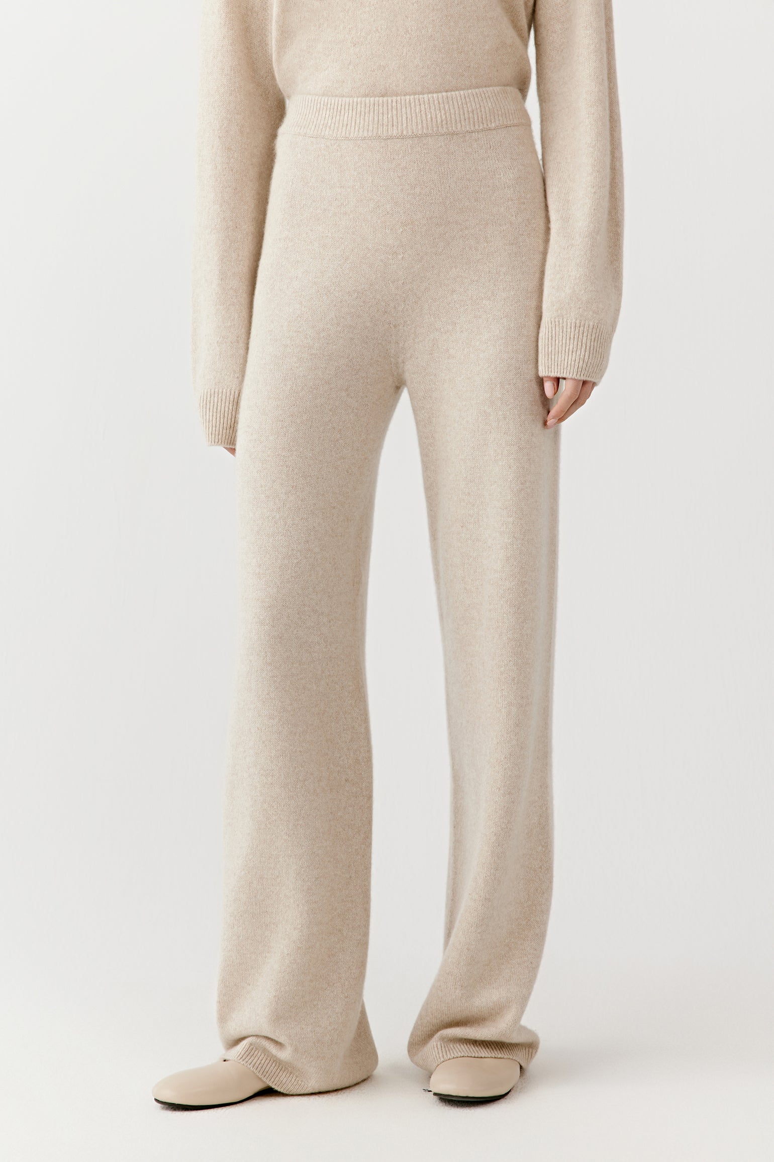 Close-up from waist to ankle showing the cream cashmere trousers’ straight-leg cut, soft texture, and clean lines.