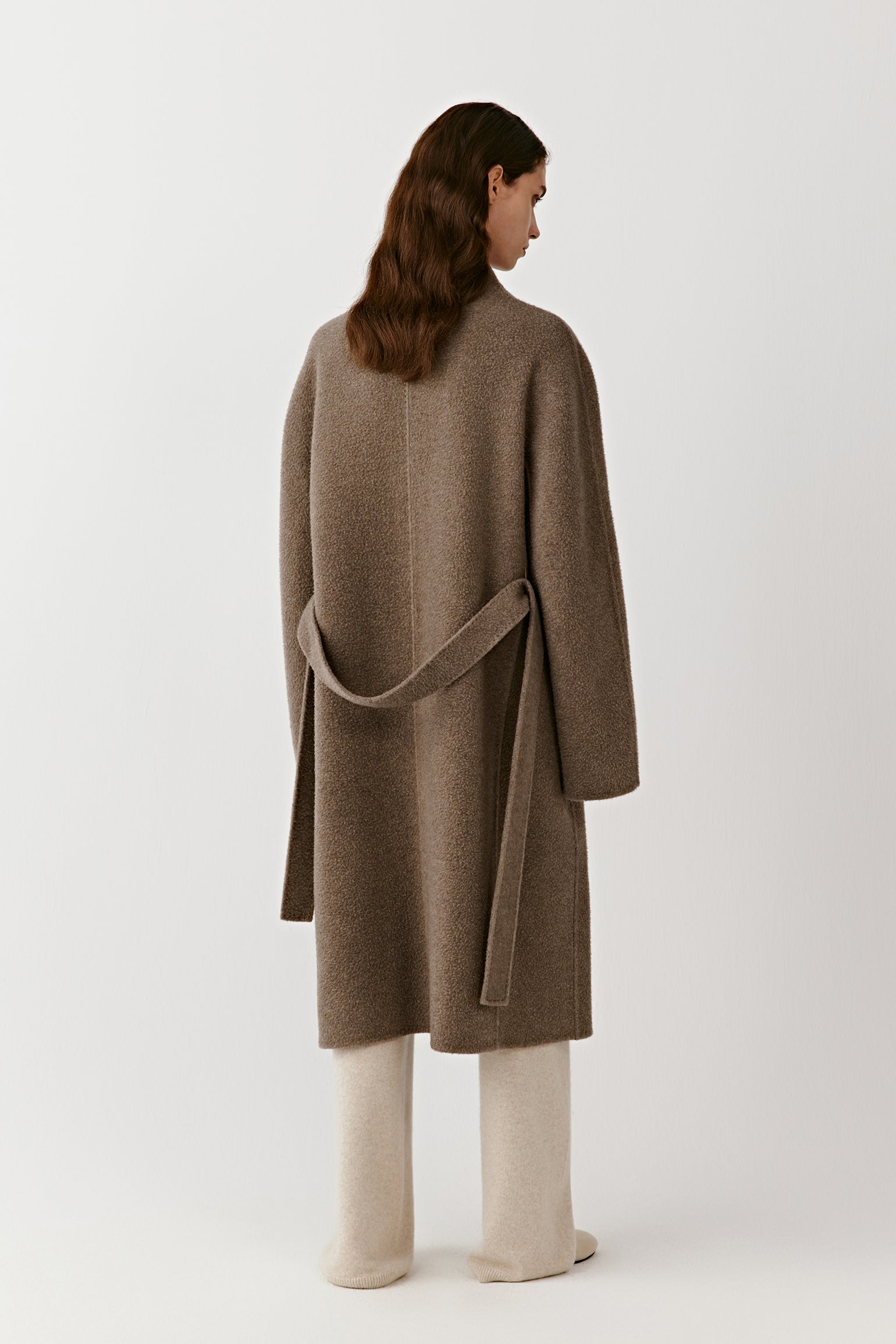 The back of the coat displays the straight, flowing lines and belt detail that enhance the coat’s minimal structure.