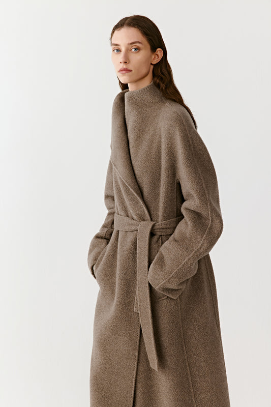The model is shown in motion, revealing the coat’s fluid drape and soft texture under natural lighting.