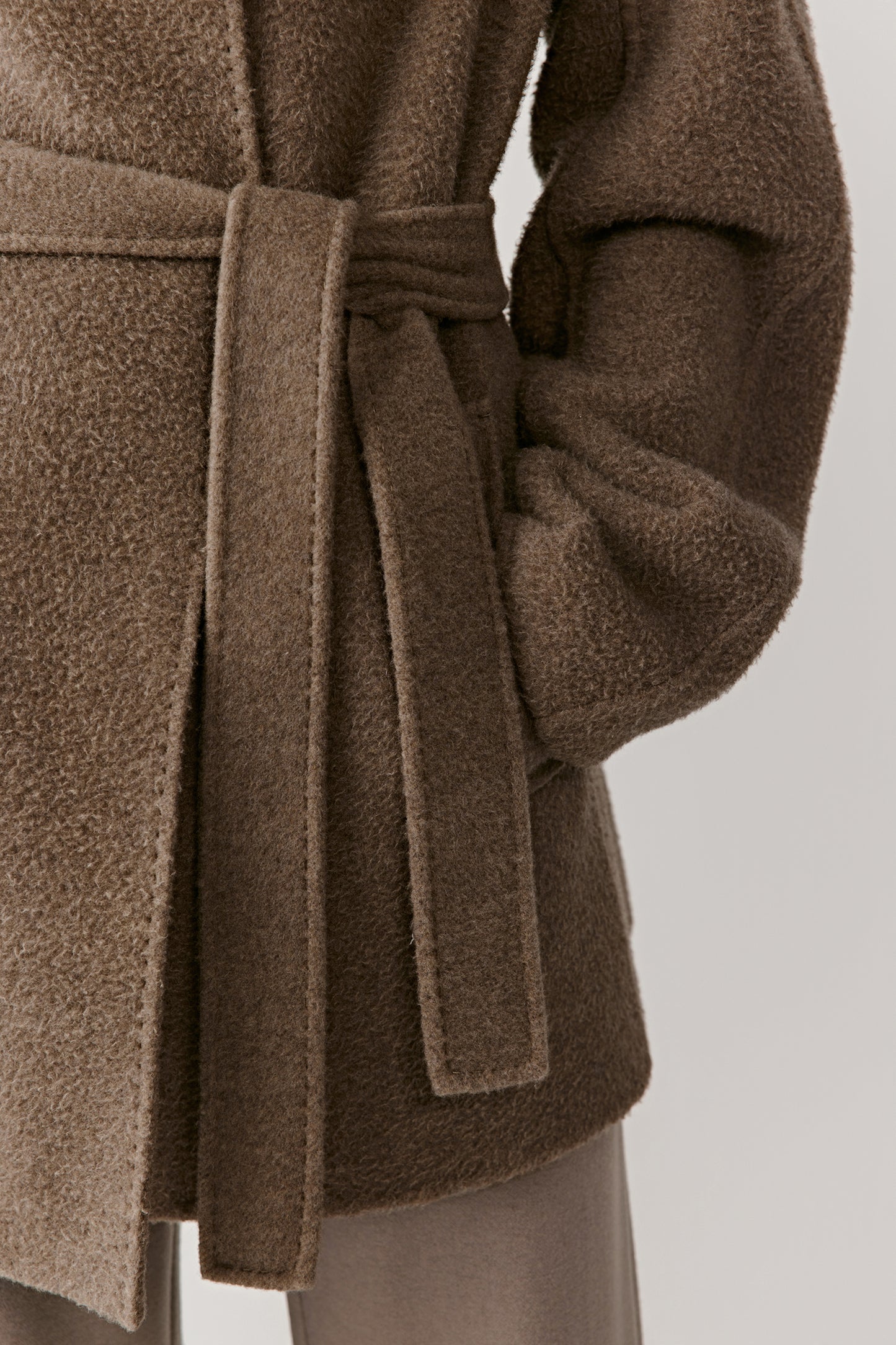 Detailed close-up of the walnut brown coat’s belt, pocket, and double-faced cashmere texture, highlighting craftsmanship and material quality.