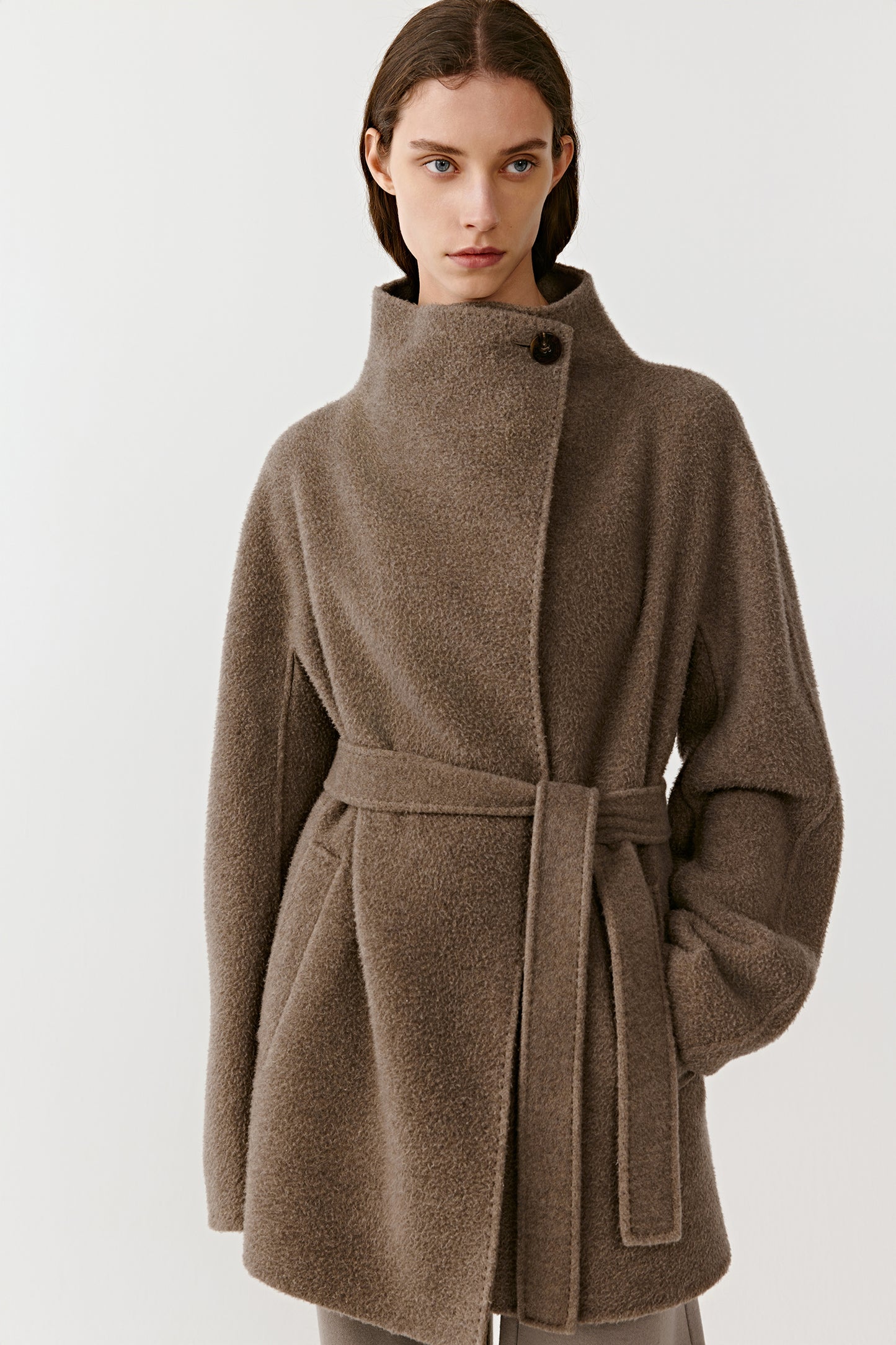 Three-quarter front view of a person wearing a brown double-faced cashmere coat, showing the belt and clean, structured lines.