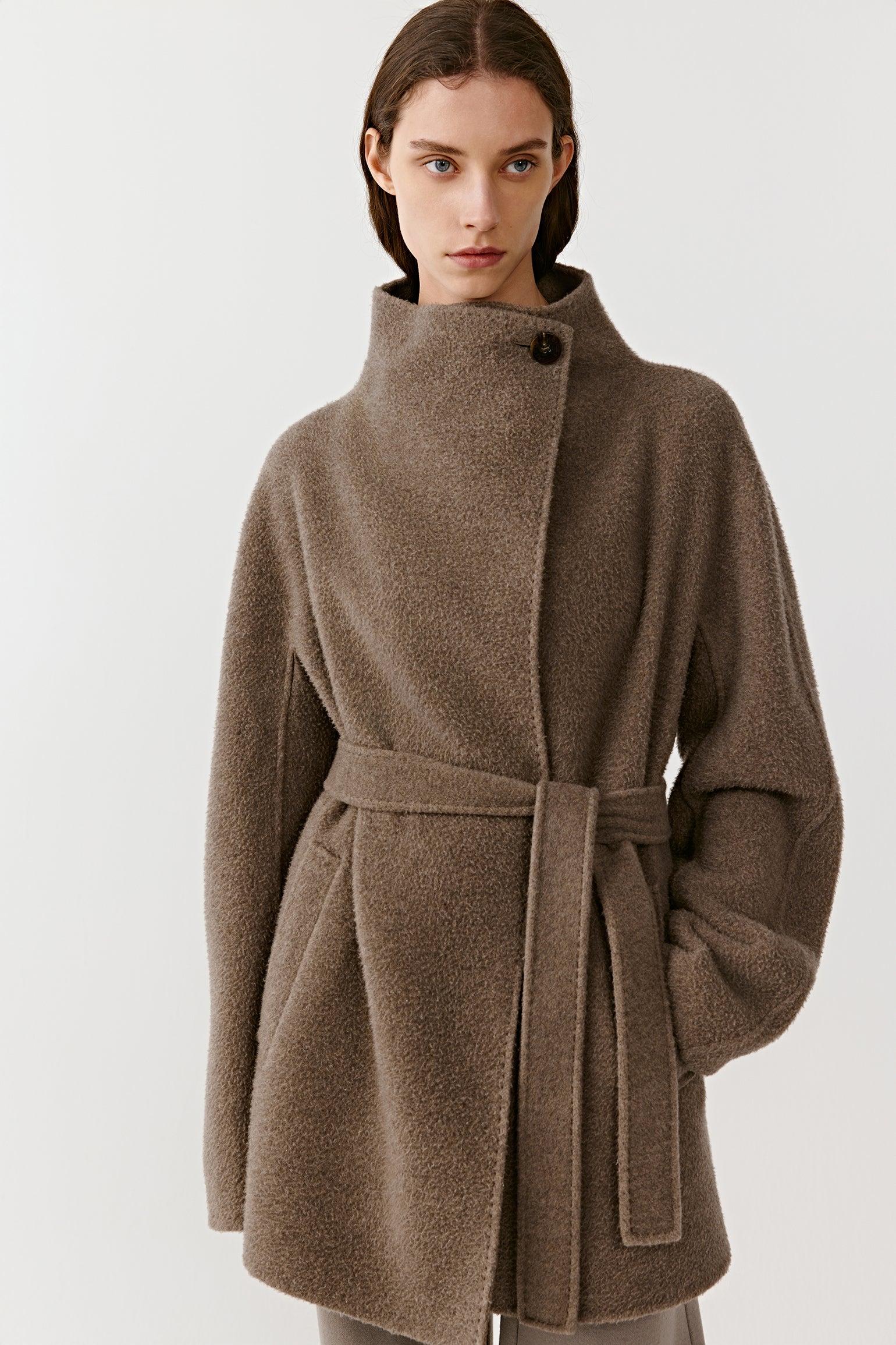 Three-quarter front view of a person wearing a brown double-faced cashmere coat, showing the belt and clean, structured lines.