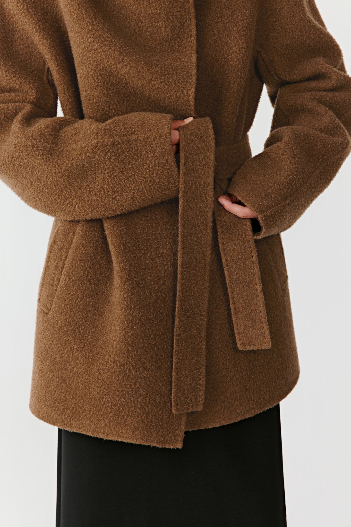Close-up of the camel and dark brown double-faced cashmere coat’s side pocket, sleeve, and tie belt, showing the detailed stitching, texture contrast, and material richness.