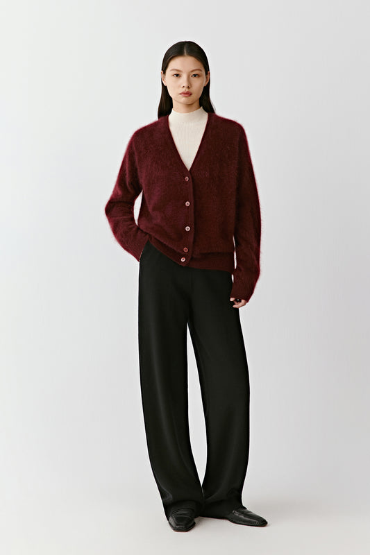 Full-length view of a person wearing a deep red cashmere cardigan with tone-on-tone buttons, paired with wide black trousers. The model stands in front of a neutral background.
