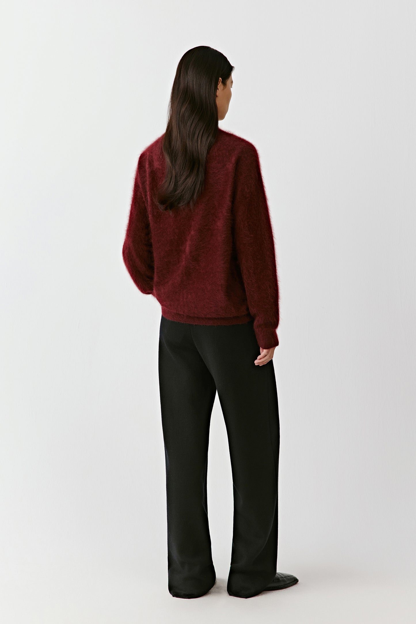 Full-body view of a person wearing a deep red cashmere cardigan, shown from a side or back angle to highlight the drape and structure of the knit.
