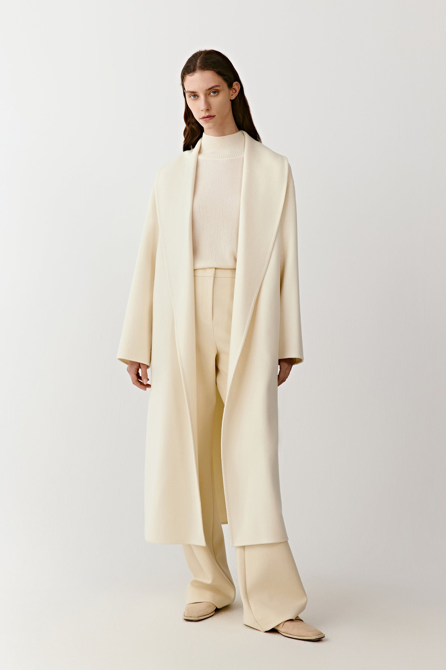 Full-length front view of a long double-faced cashmere coat with a shawl collar and matching belt in a natural undyed shade.