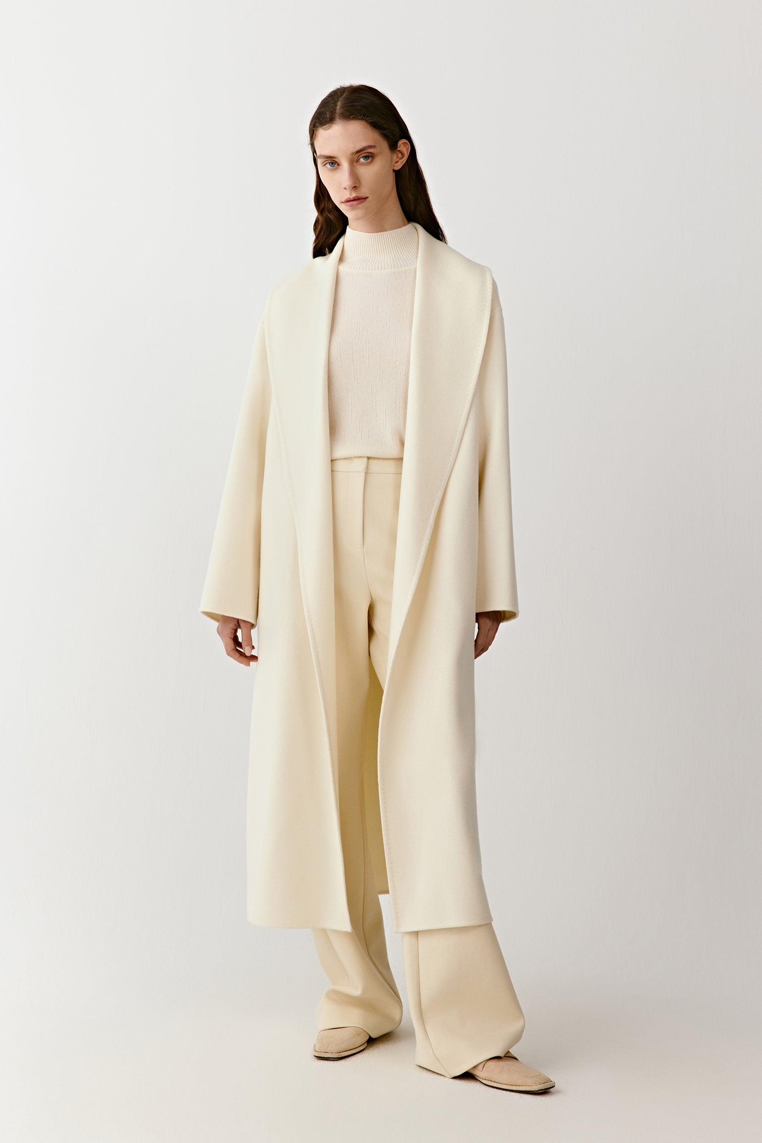 Full-length front view of a long double-faced cashmere coat with a shawl collar and matching belt in a natural undyed shade.