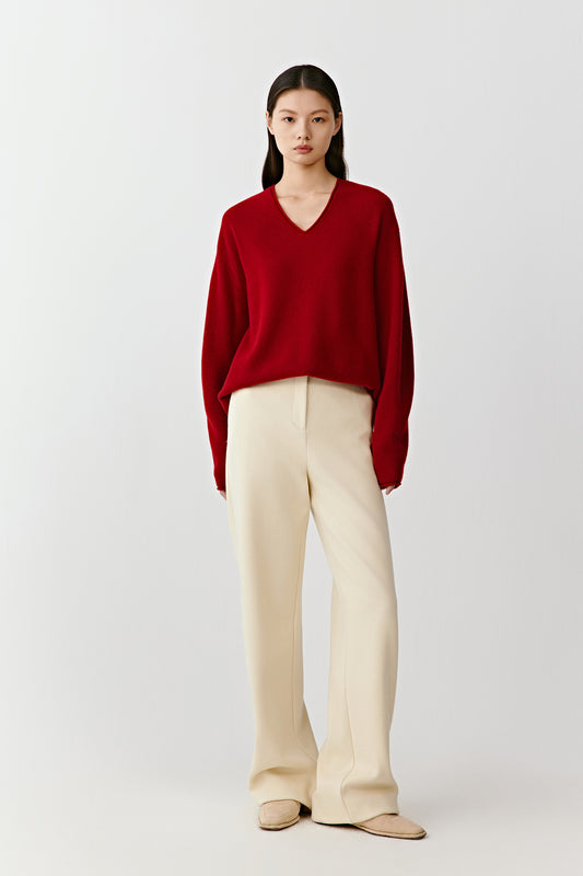 Full-length front view of a red cashmere pullover with a deep V neckline, styled with light trousers.