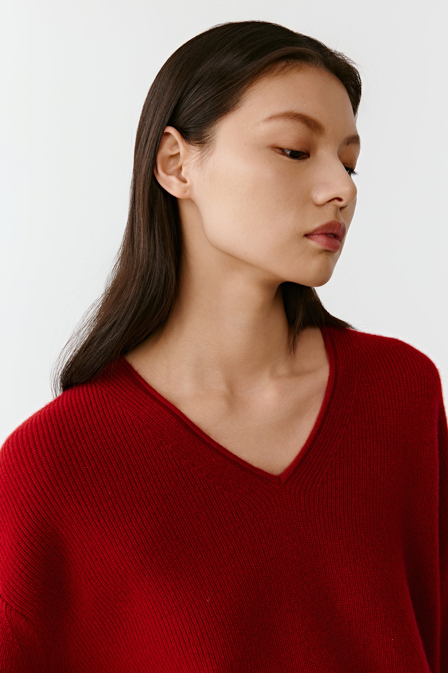 Close-up of the deep V neckline of the red cashmere pullover, revealing the fine knit and vibrant color.