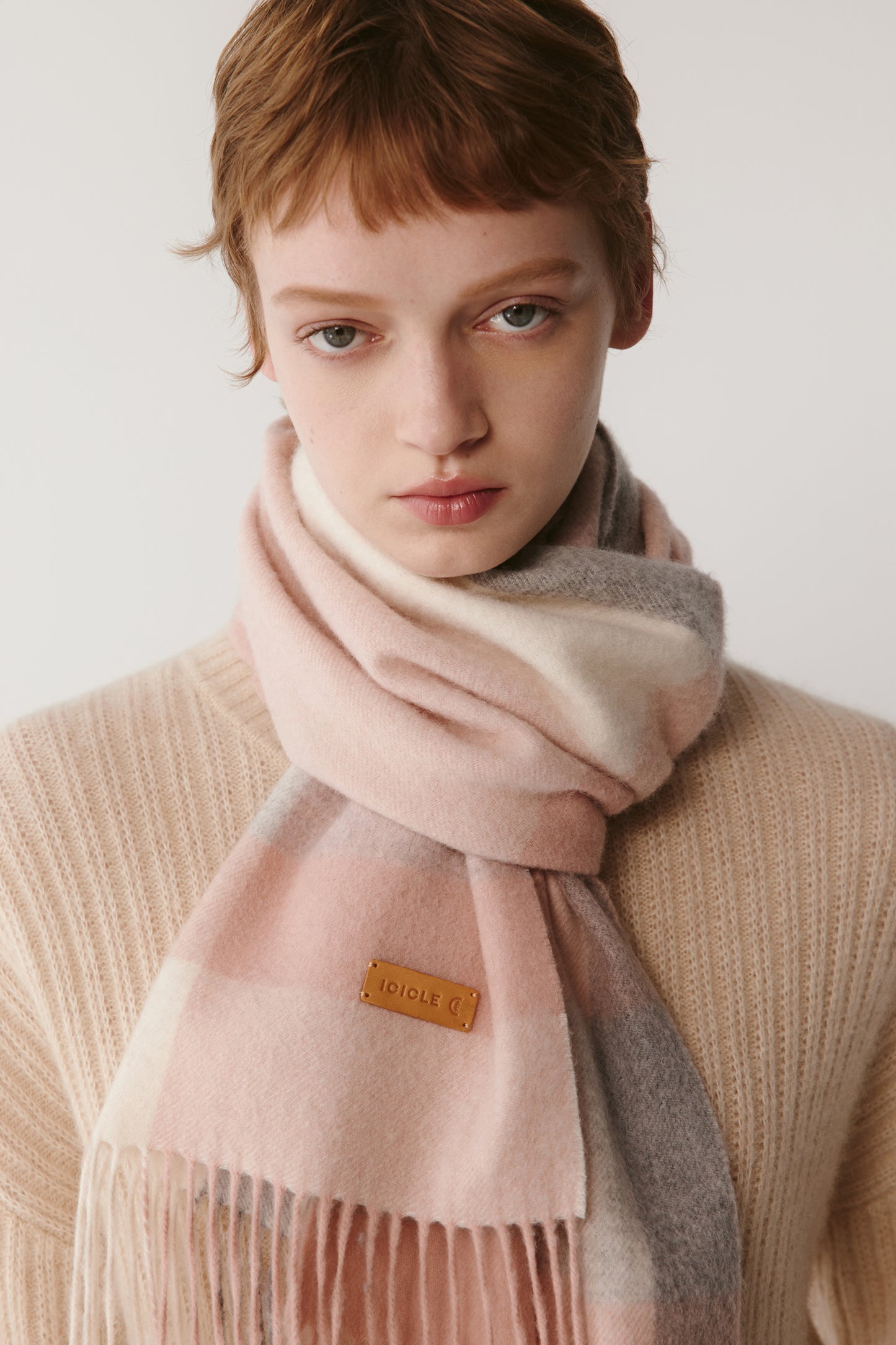 A close-up of a woman wearing a pink checked cashmere scarf, showing the soft texture and pastel tones.