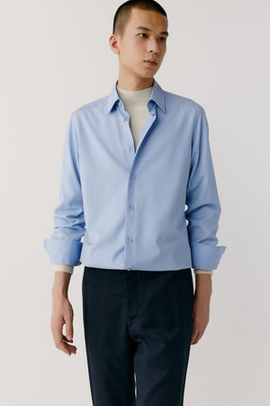 Man wearing a light blue merino wool shirt with relaxed straight fit and square collar, styled with dark trousers, front three-quarter view.