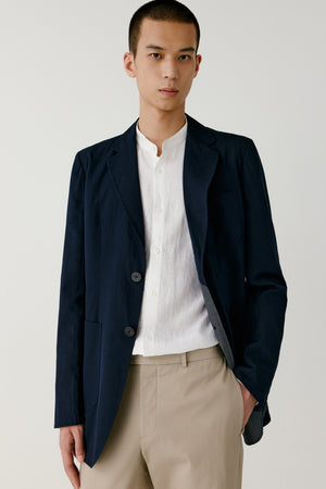 Man wearing a navy double-face cotton blazer with straight fit, styled with beige trousers and white T-shirt, front portrait view.