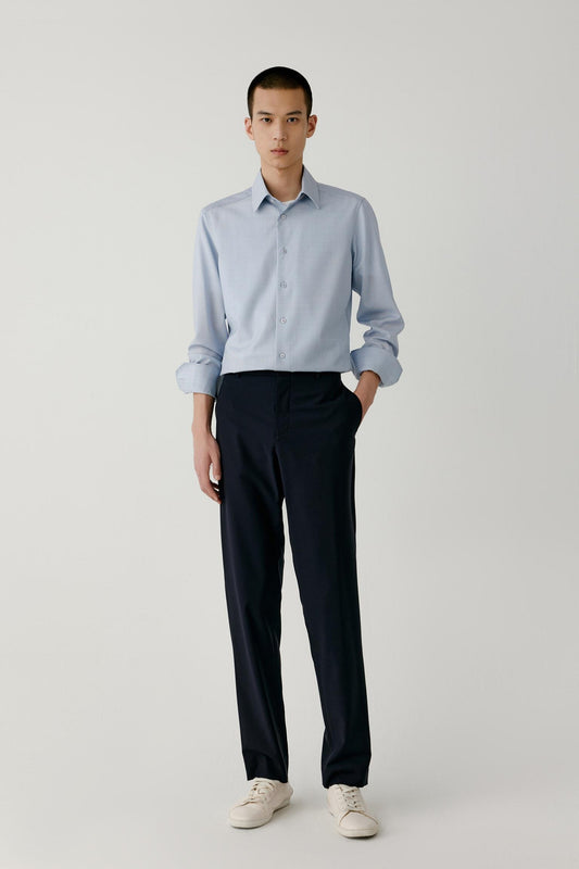 Full-length view of a man wearing a light blue checked worsted wool shirt, highlighting the straight cut and curved hem.
