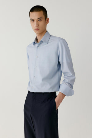 Front view of a man wearing a light blue checked worsted wool shirt, showing the straight silhouette and pointed collar.
