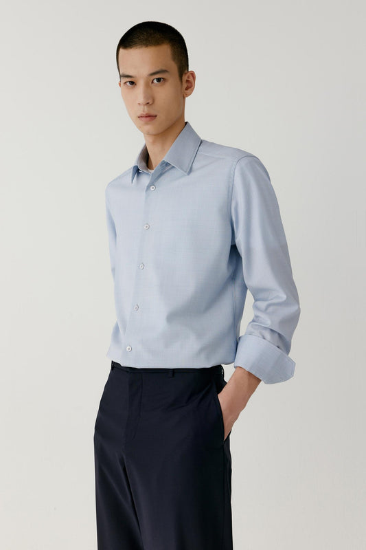 Front view of a man wearing a light blue checked worsted wool shirt, showing the straight silhouette and pointed collar.