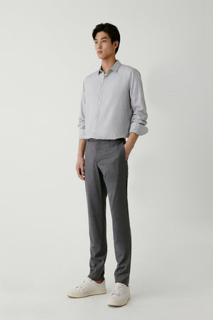 Man wearing light grey slim-fit wool trousers with a tapered tailored cut, styled with a light blue shirt, full-length front view.
