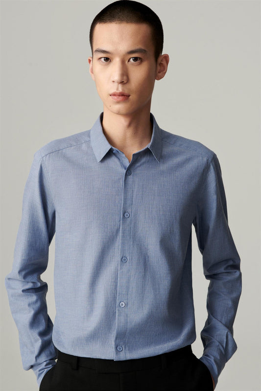 Front view of a man wearing a light blue cotton shirt, showing the straight silhouette, pointed collar and button-front fastening.