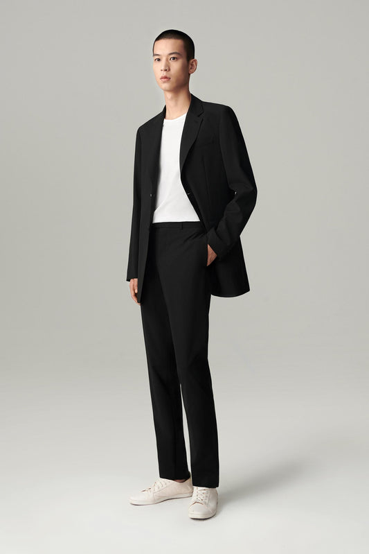 Front view of a man wearing a black wool blazer, showing the elongated straight silhouette and notched lapels.