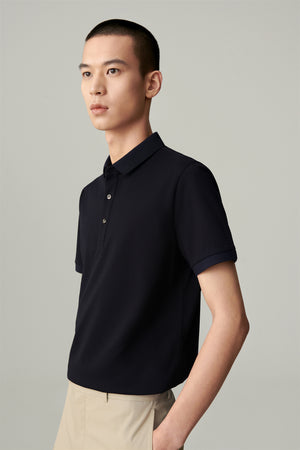 Man wearing a navy blue piqué cotton polo shirt with a slim straight fit, styled with beige trousers, portrait front view highlighting the polo collar and button placket.