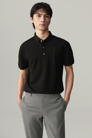 Front view of a man wearing a deep black silk polo, showing the straight silhouette, polo collar and three-button placket.