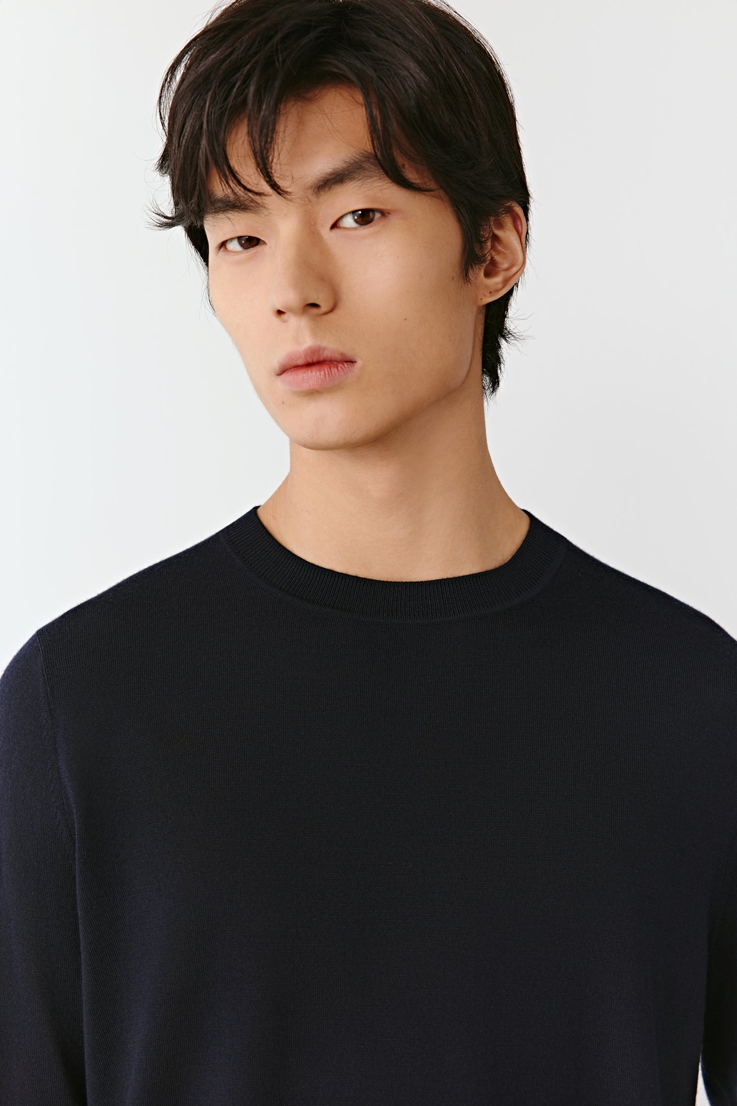 Man wearing a blue-black fine merino wool jumper with a straight, relaxed fit; close-up portrait highlighting the clean crew neckline, smooth knit texture and even finish across the shoulders and chest.