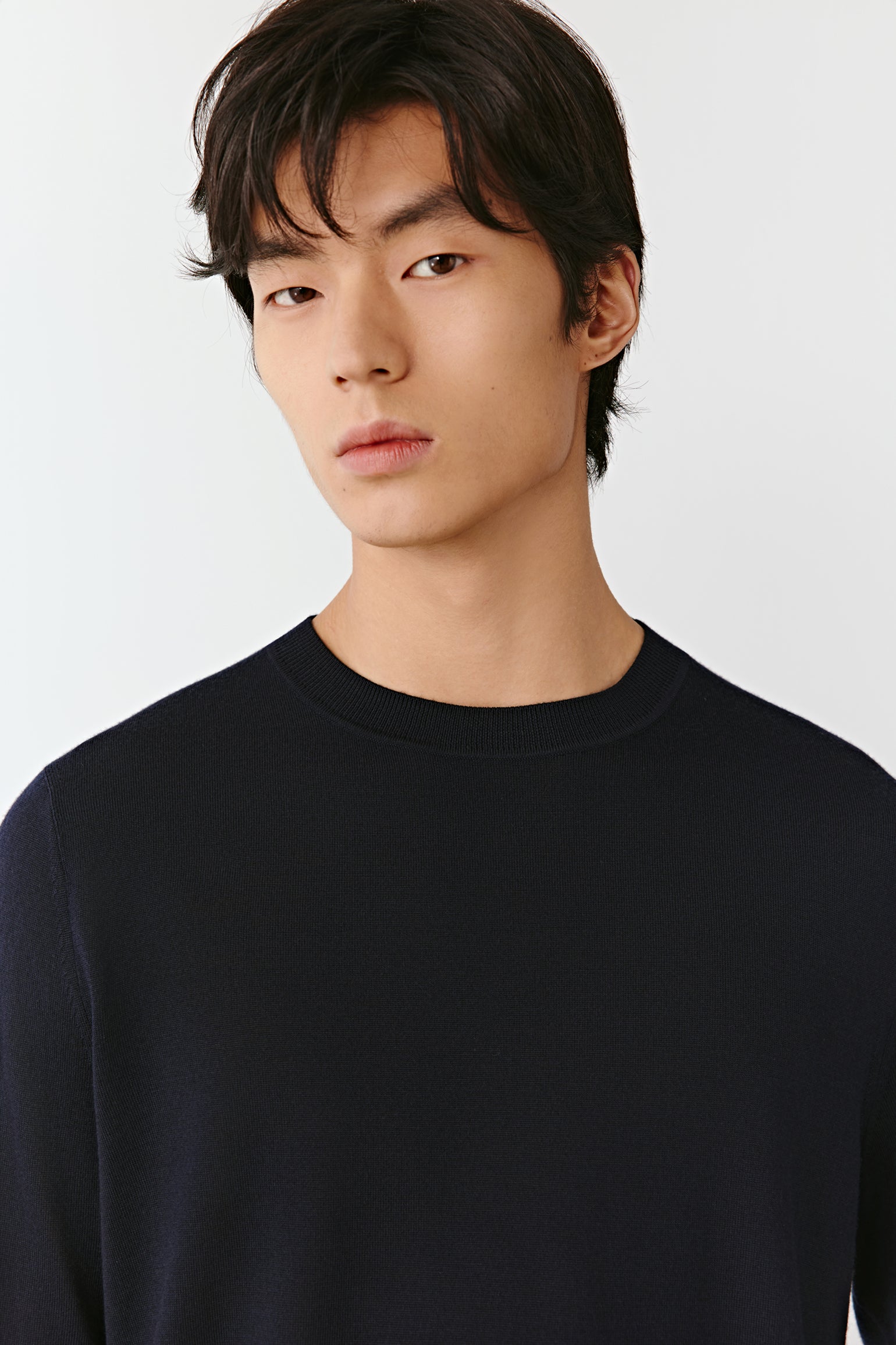 Man wearing a blue-black fine merino wool jumper with a straight, relaxed fit; close-up portrait highlighting the clean crew neckline, smooth knit texture and even finish across the shoulders and chest.